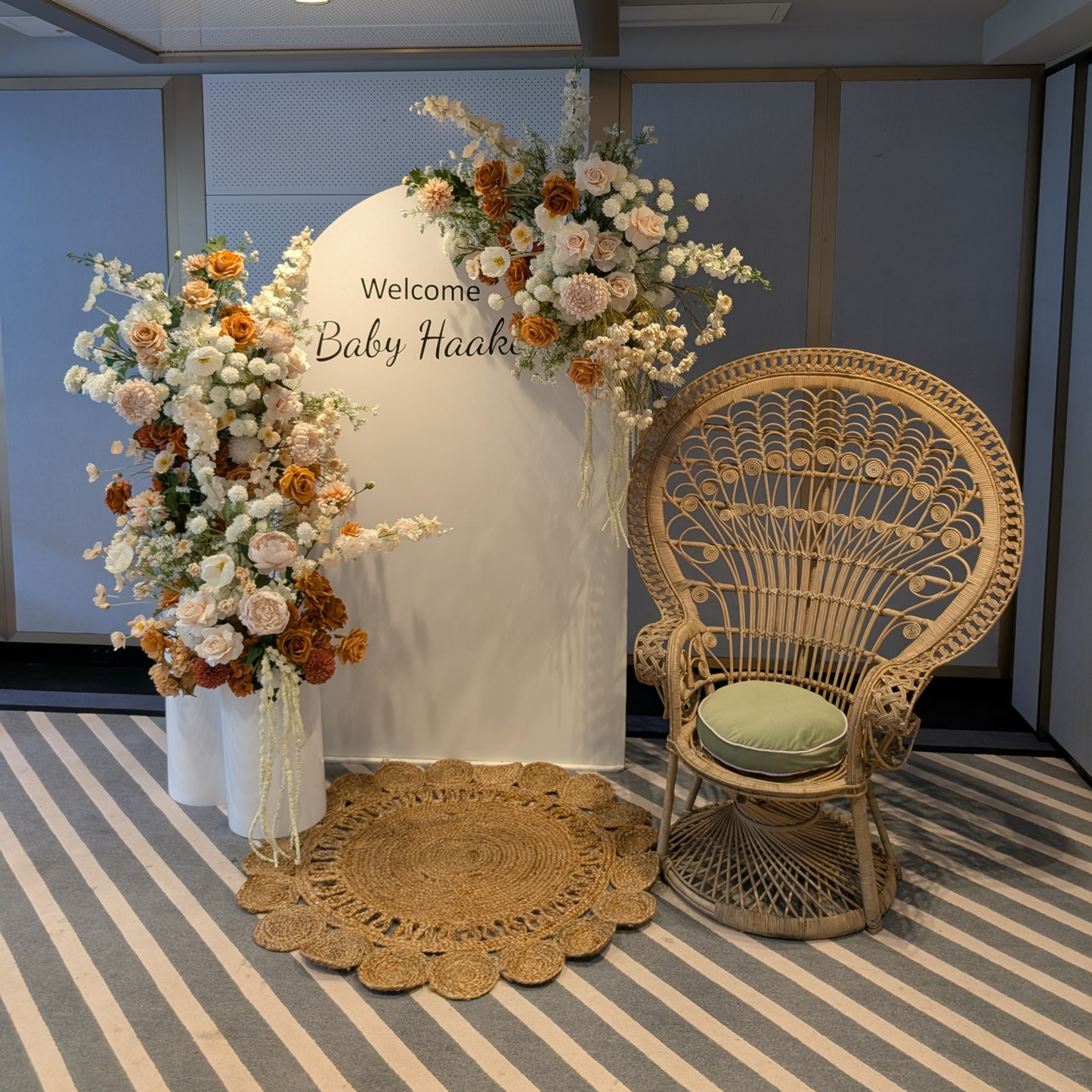 Decorative setup with floral arch, wicker chair, and round mat on a striped floor.