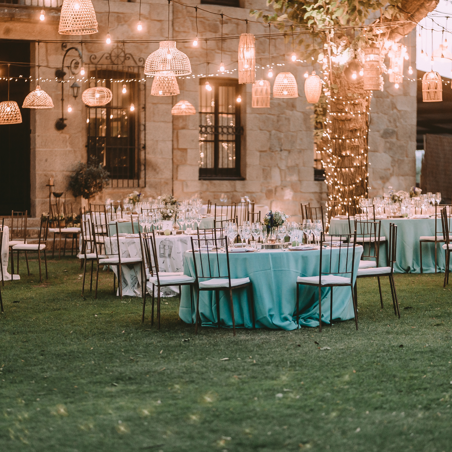 An outdoor wedding reception with round tables covered in teal tablecloths and white chairs. The tables are decorated with floral centerpieces and lit by string lights hanging from the trees. Prop hire, Prop hiring, Prop hire, event stylists Brisbane, brisbane event styling, brisbane event styling, event stylist Brisbane, Brisbane Wedding, Gold Coast Wedding, Floral Styling, Lush & Lavish Events, Brisbane Tablescape, Gold Coast Tablescapes, Brisbane Candle Hire