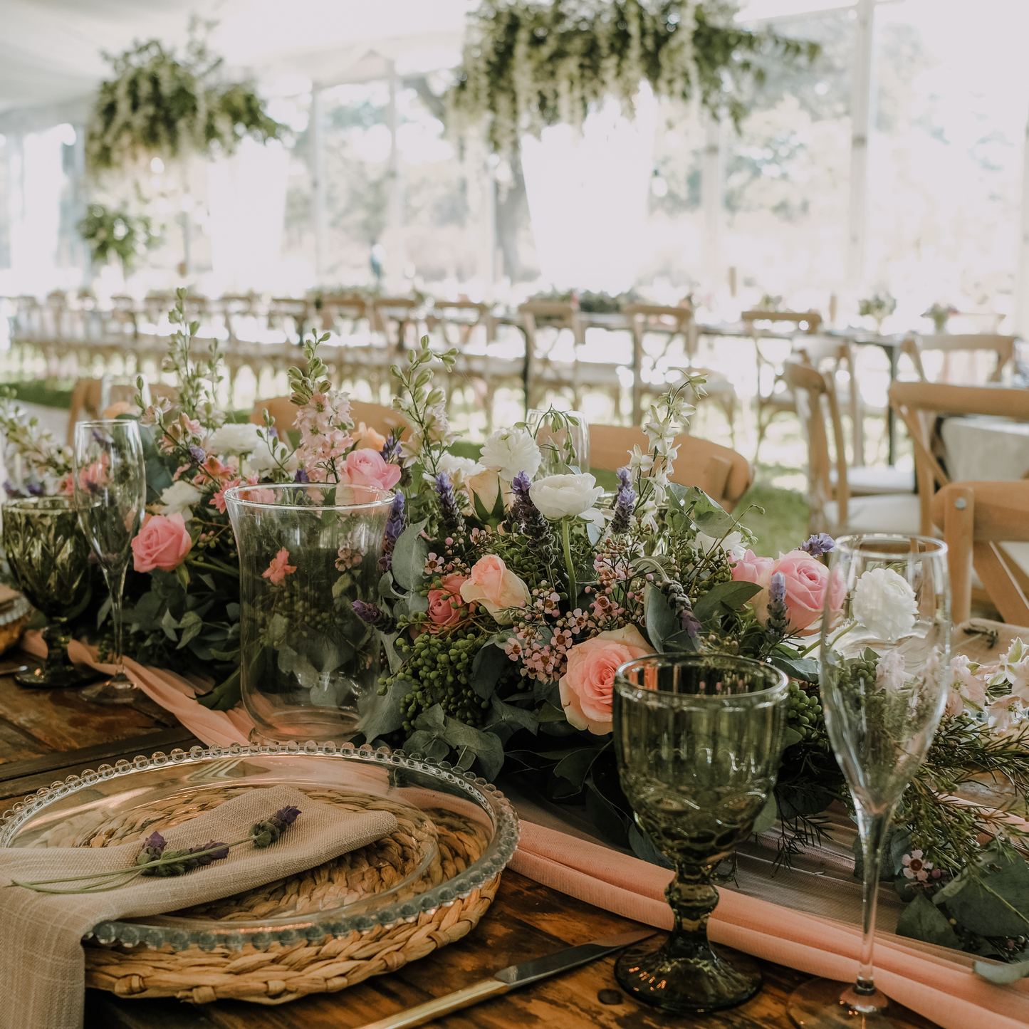 Elegantly set table with pink and white floral centerpiece, clear glass goblets, and woven placemats. Other similarly decorated tables are visible in an outdoor tent setting. Prop hire, Prop hiring, Prop hire, event stylists Brisbane, brisbane event styling, brisbane event styling, event stylist Brisbane, Brisbane Wedding, Gold Coast Wedding, Floral Styling, Lush & Lavish Events, Brisbane Tablescape, Gold Coast Tablescapes