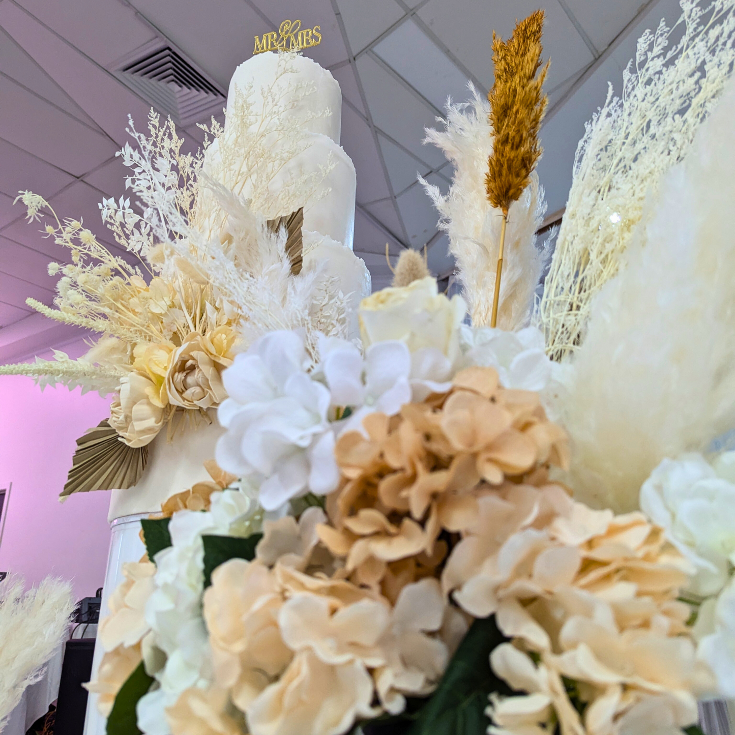 Cake with white and gold icing, adorned with white, cream, and pale gold flowers, topped with a ‘Mr & Mrs’ sign, surrounded by golden stalks and white foliage. Prop hire, Prop hiring, Prop hire, event stylists Brisbane, brisbane event styling, brisbane event styling, event stylist Brisbane, Brisbane Wedding, Gold Coast Wedding, Floral Styling, Lush & Lavish Events, Brisbane Tablescape, Gold Coast Tablescapes, Brisbane Candle Hire