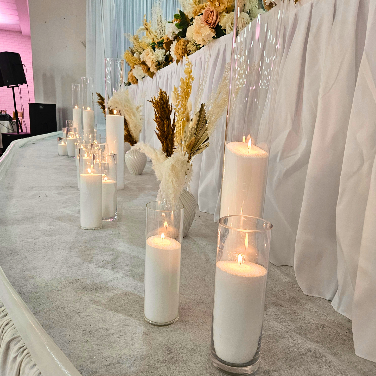 Lit candles in clear glass holders on a white-draped table with boho floral arrangements. Sheer curtain backdrop adds a romantic ambiance. Prop hire, Prop hiring, Prop hire, event stylists Brisbane, brisbane event styling, brisbane event styling, event stylist Brisbane, Brisbane Wedding, Gold Coast Wedding, Floral Styling, Lush & Lavish Events, Brisbane Tablescape, Gold Coast Tablescapes, Brisbane Candle Hire