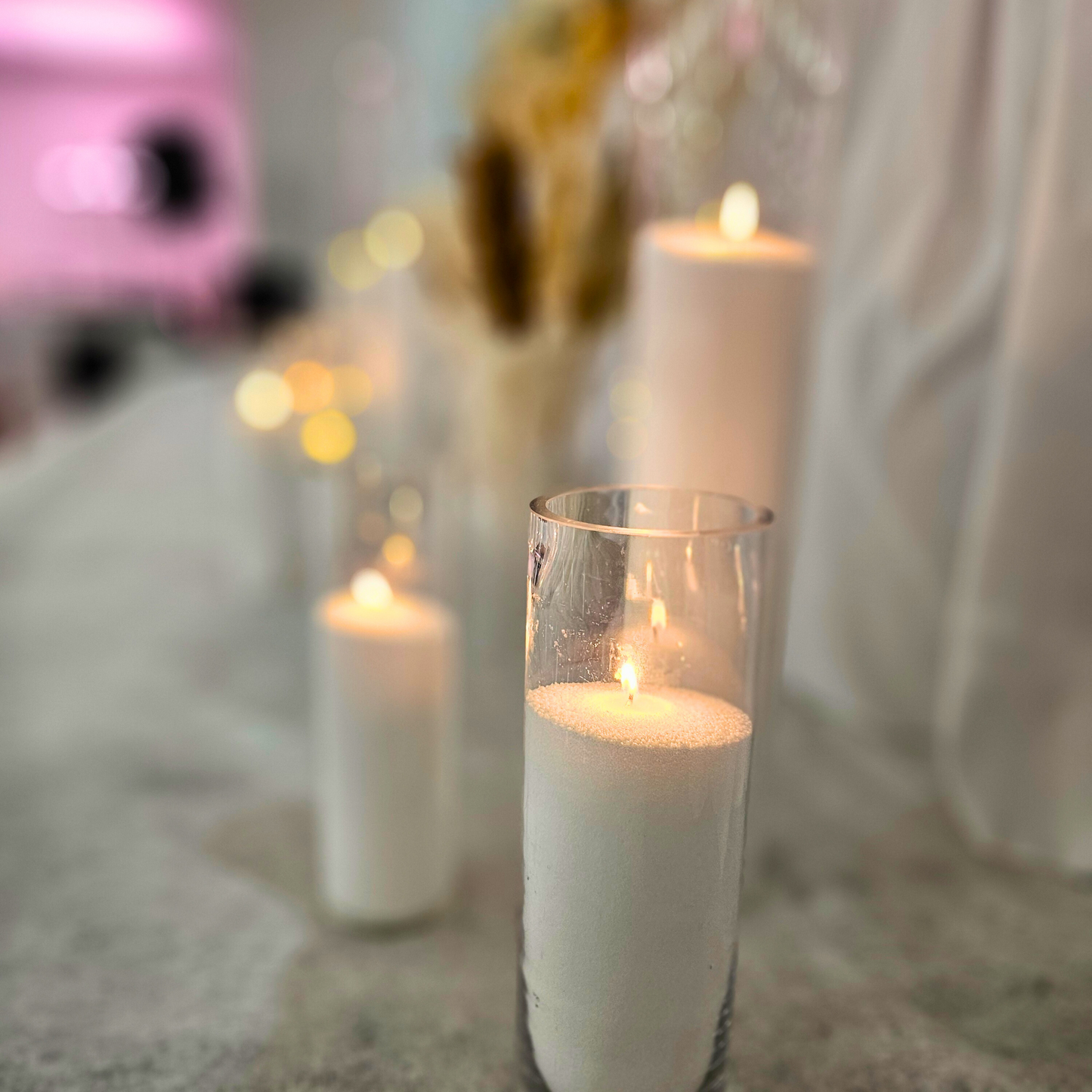 Close-up of lit candles in tall glass holders against a blurred bridal table with boho decorations, creating an intimate, romantic ambiance. Prop hire, Prop hiring, Prop hire, event stylists Brisbane, brisbane event styling, brisbane event styling, event stylist Brisbane, Brisbane Wedding, Gold Coast Wedding, Floral Styling, Lush & Lavish Events, Brisbane Tablescape, Gold Coast Tablescapes, Brisbane Candle Hire