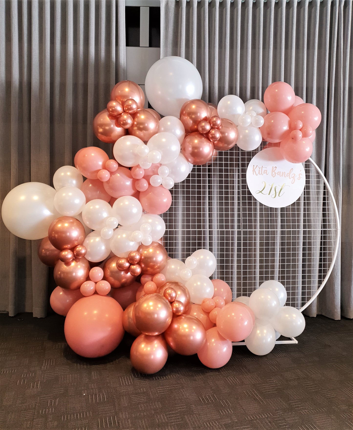 A large balloon garland in shades of pink and white hangs on a circular metal frame with a sign that says "Kita Bandz's 21st." Prop hire, Prop hiring, Prop hire, event stylists Brisbane, brisbane event styling, brisbane event styling, event stylist Brisbane, Brisbane Wedding, Gold Coast Wedding, Floral Styling, Lush & Lavish Events, Brisbane Tablescape, Gold Coast Tablescapes, Brisbane Candle Hire