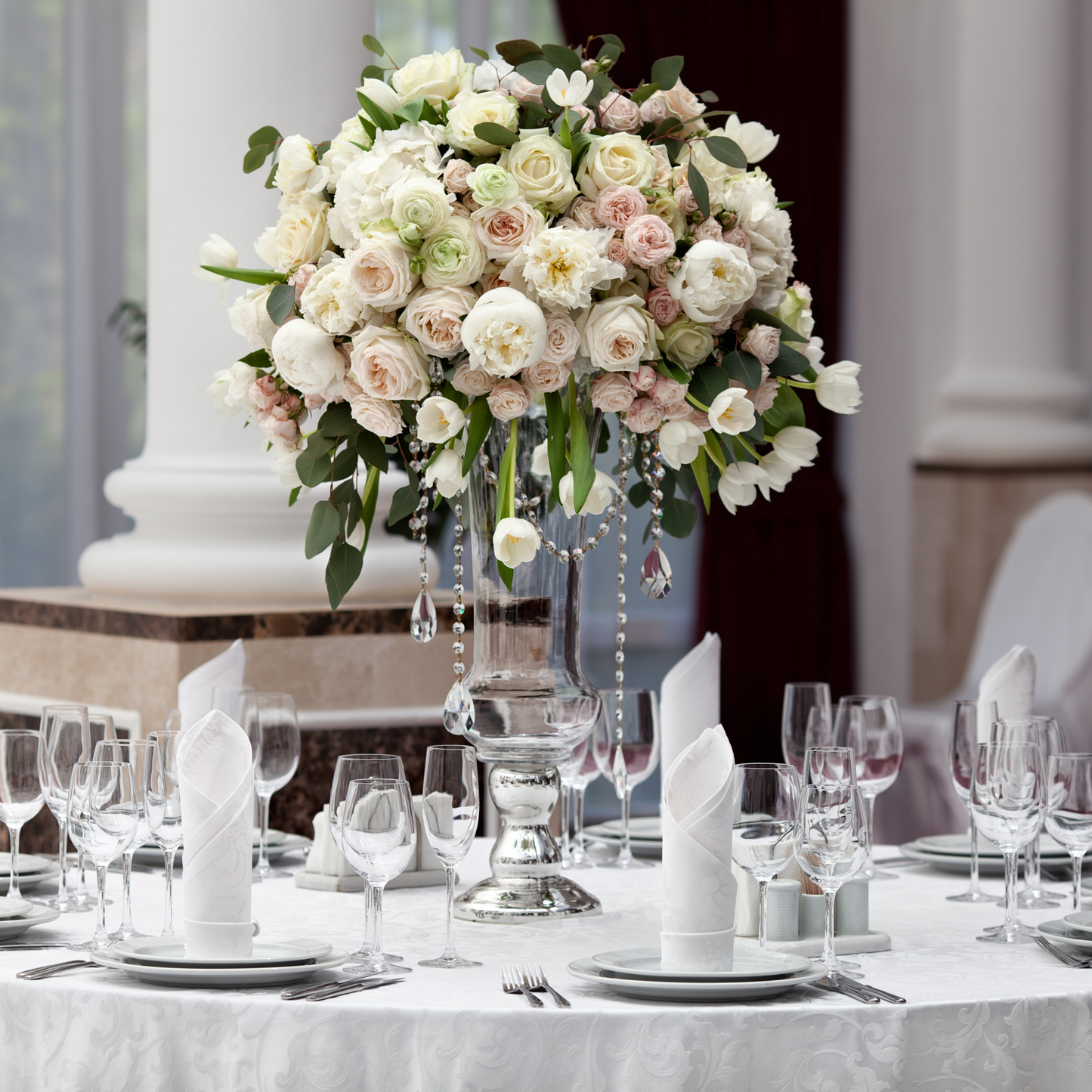 A large, elegant centerpiece of white and pink roses sits at the center of a round dining table. The table is set with white tablecloths, white plates, and silver cutlery. Prop hire, Prop hiring, Prop hire, event stylists Brisbane, brisbane event styling, brisbane event styling, event stylist Brisbane, Brisbane Wedding, Gold Coast Wedding, Floral Styling, Lush & Lavish Events, Brisbane Tablescape, Gold Coast Tablescapes, Brisbane Candle Hire