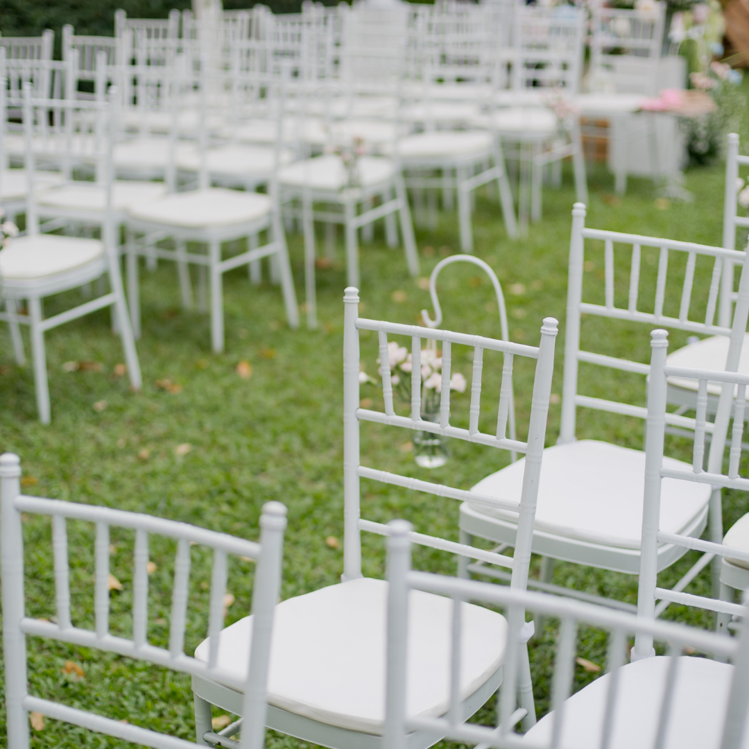 Outdoor event setup with neatly arranged rows of white chairs on a grassy lawn, likely for a wedding or ceremony, with small flower arrangements hanging from some chairs. Prop hire, Prop hiring, Prop hire, event stylists Brisbane, brisbane event styling, brisbane event styling, event stylist Brisbane, Brisbane Wedding, Gold Coast Wedding, Floral Styling, Lush & Lavish Events, Brisbane Tablescape, Gold Coast Tablescapes, Brisbane Candle Hire