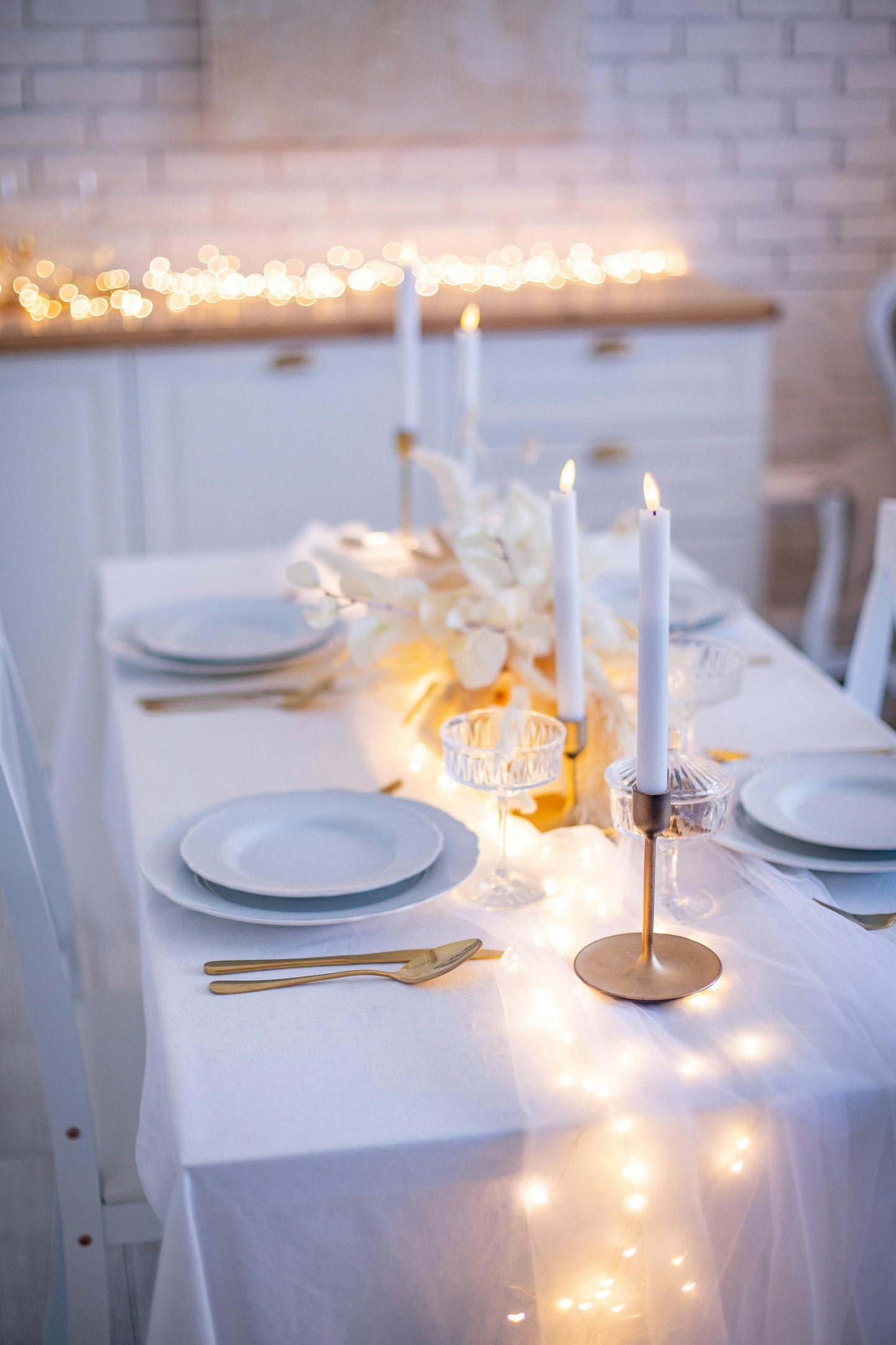 A long rectangular table with a white tablecloth set for a festive occasion, decorated with white candles, a floral centerpiece, and string lights. Prop hire, Prop hiring, Prop hire, event stylists Brisbane, brisbane event styling, brisbane event styling, event stylist Brisbane, Brisbane Wedding, Gold Coast Wedding, Floral Styling, Lush & Lavish Events, Brisbane Tablescape, Gold Coast Tablescapes, Brisbane Candle Hire