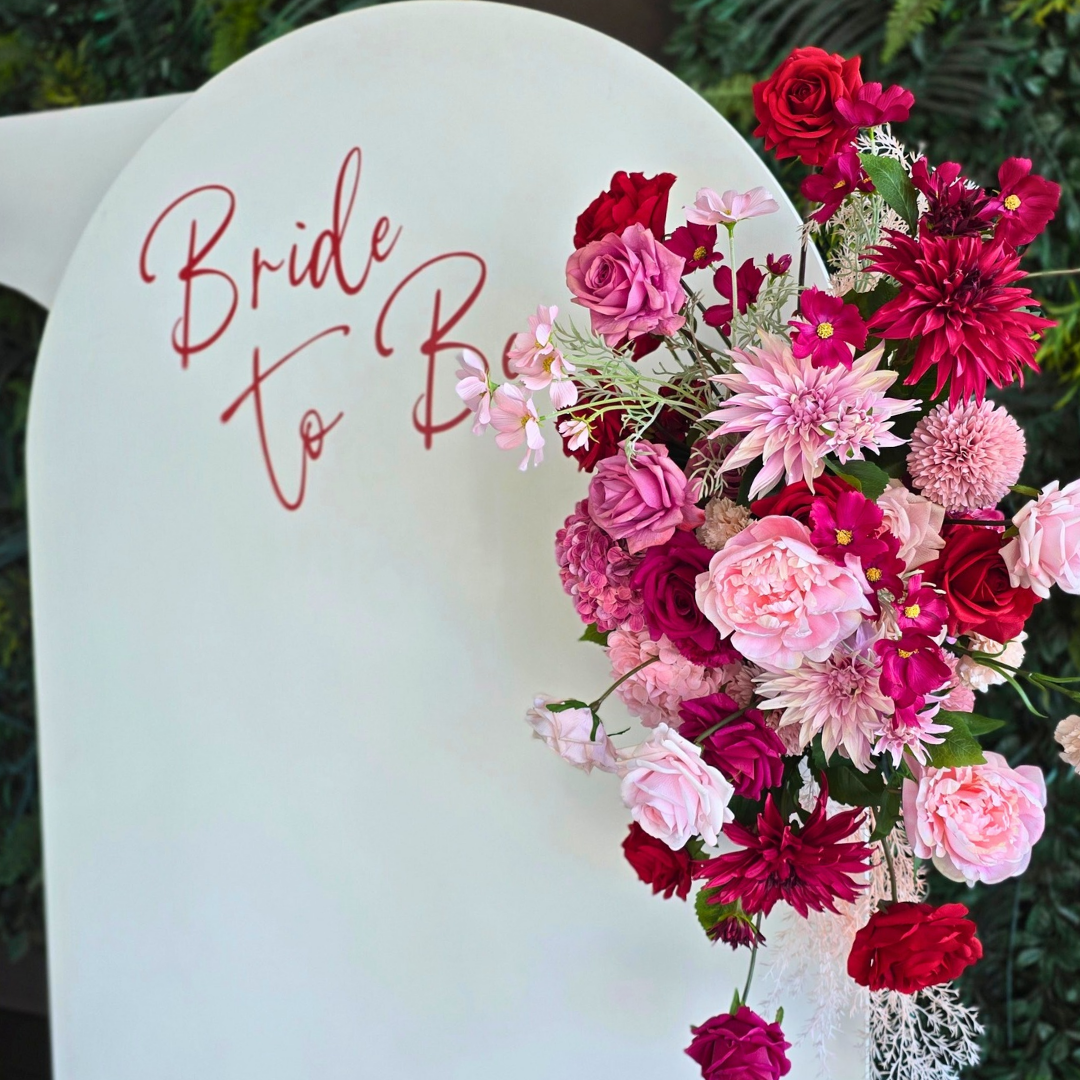 Floral arrangement with 'Bride To Be' text on a white background. bridal shower backdrop, red and pink floral backdrop, elegant event styling, wedding backdrop hire, engagement party decor, Brisbane event hire, floral arch setup, romantic party backdrop, custom event decor, luxe bridal shower decorations