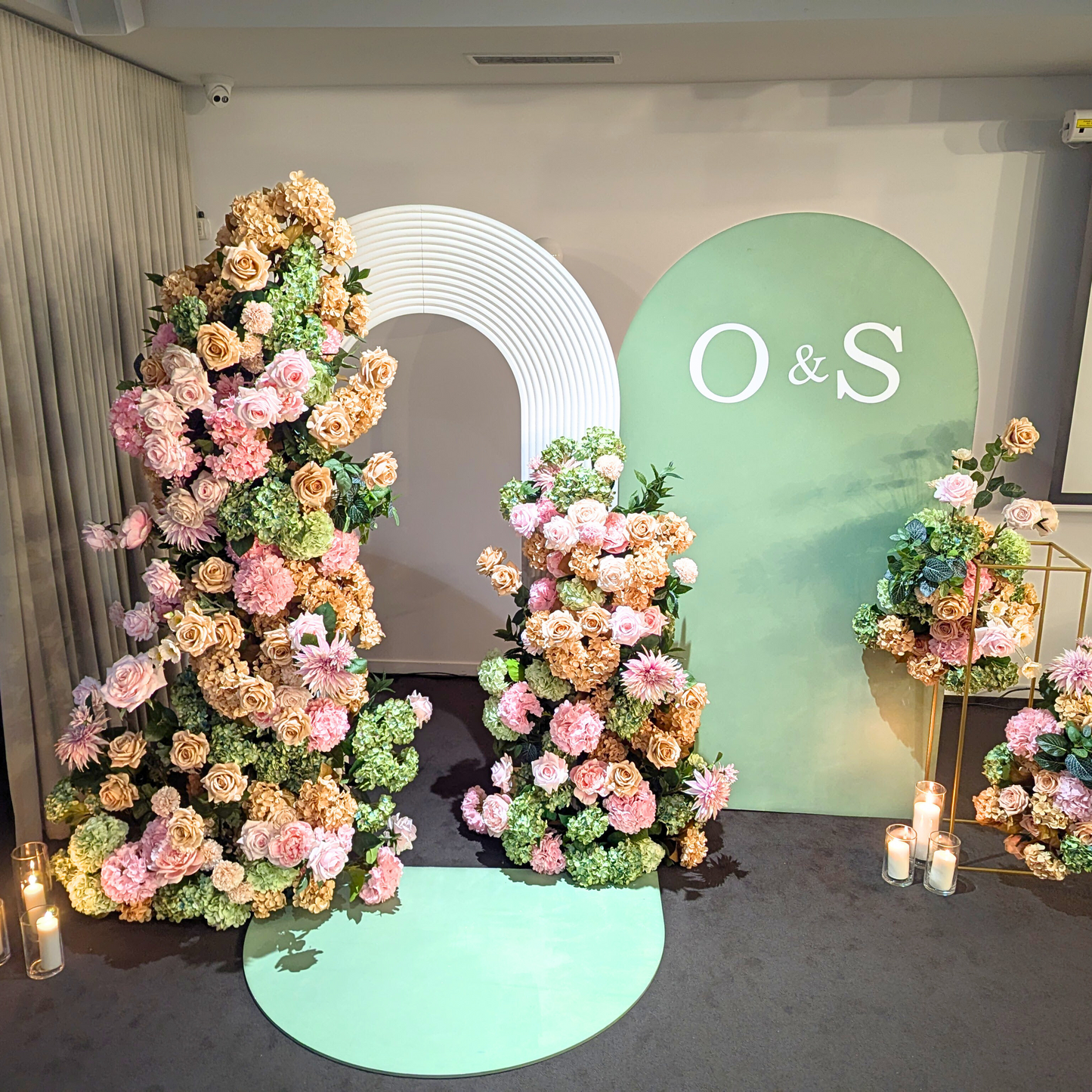 Wedding backdrop with a large white circular arch, initials ‘O&S,’ pink, peach, and cream roses, green floor mat, and lit candles on gold stands. Prop hire, Prop hiring, Prop hire, event stylists Brisbane, brisbane event styling, brisbane event styling, event stylist Brisbane, Brisbane Wedding, Gold Coast Wedding, Floral Styling, Lush & Lavish Events, Brisbane Tablescape, Gold Coast Tablescapes, Brisbane Candle Hire