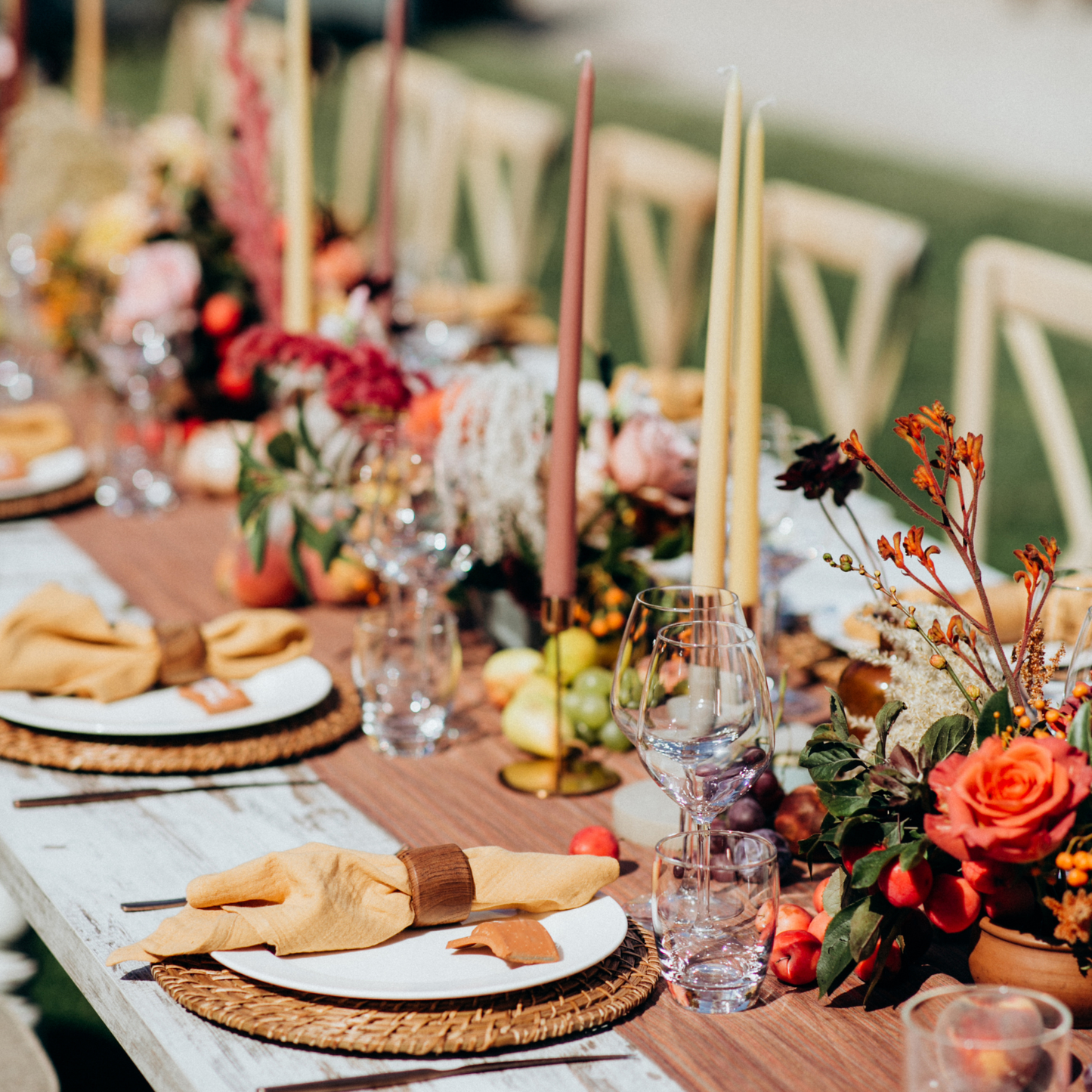 Outdoor dining table with tall candles, floral arrangements, and fruits, set with white plates, yellow napkins, and clear glasses on woven placemats. Wooden cross-back chairs add to the rustic theme. Prop hire, Prop hiring, Prop hire, event stylists Brisbane, brisbane event styling, brisbane event styling, event stylist Brisbane, Brisbane Wedding, Gold Coast Wedding, Floral Styling, Lush & Lavish Events, Brisbane Tablescape, Gold Coast Tablescapes, Brisbane Candle Hire
