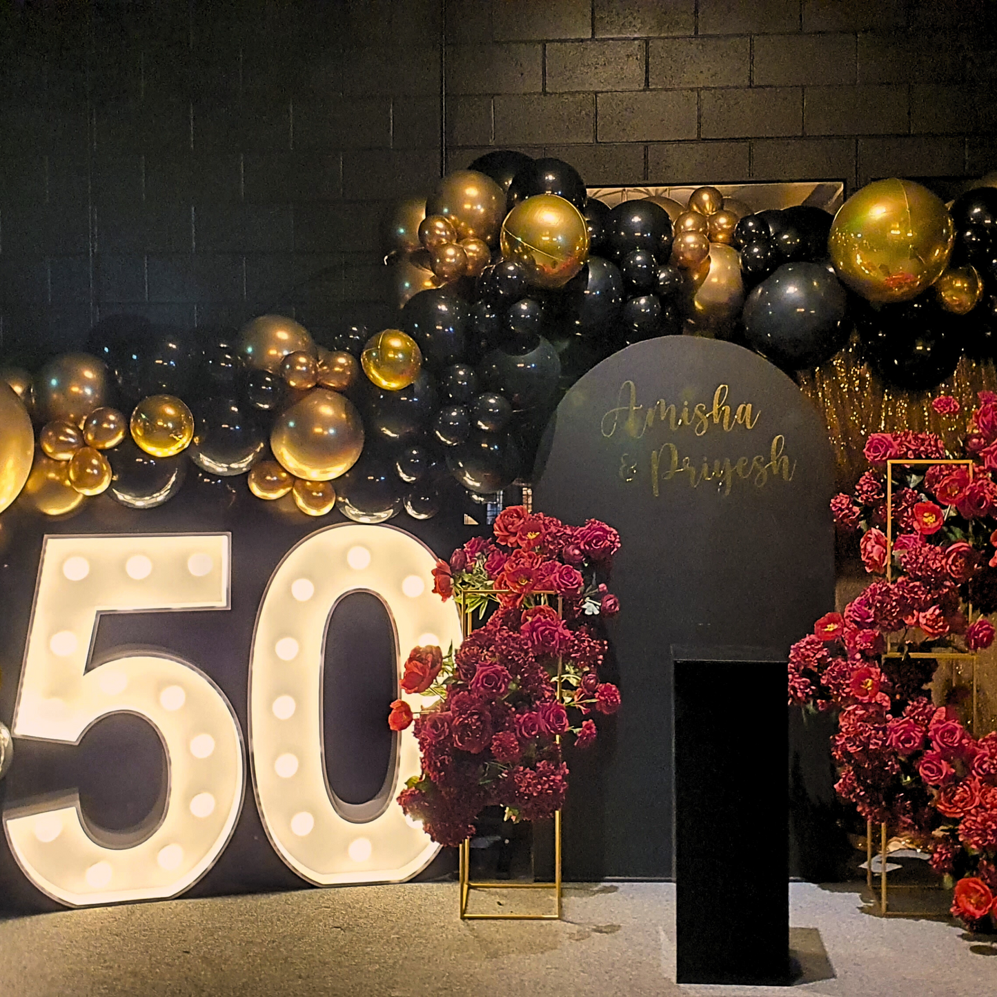 White '50' with light bulbs, black and gold balloons, black sign with 'Amisha & Priyesh,' deep red flowers, and golden elements. Prop hire, Prop hiring, Prop hire, event stylists Brisbane, brisbane event styling, brisbane event styling, event stylist Brisbane, Brisbane Wedding, Gold Coast Wedding, Floral Styling, Lush & Lavish Events, Brisbane Tablescape, Gold Coast Tablescapes, Brisbane Candle Hire