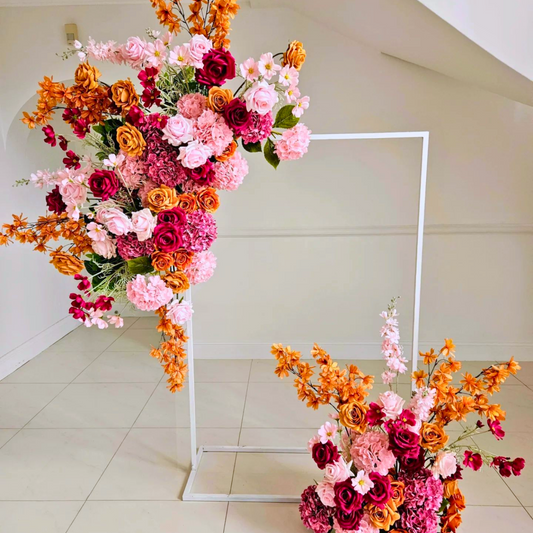 Floral arrangement of pink, orange, and yellow roses and lilies on a white frame, with densely packed flowers in the top left and bottom right corners. Prop hire, Prop hiring, Prop hire, event stylists Brisbane, brisbane event styling, brisbane event styling, event stylist Brisbane, Brisbane Wedding, Gold Coast Wedding, Floral Styling, Lush & Lavish Events, Brisbane Tablescape, Gold Coast Tablescapes, Brisbane Candle Hire