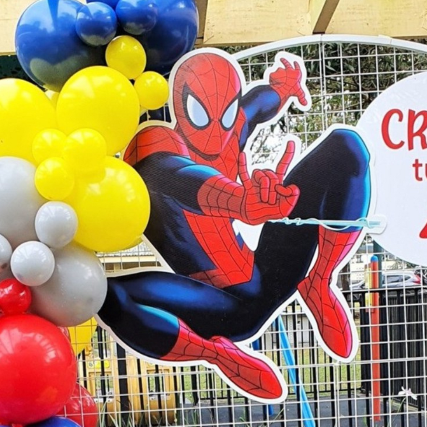 A Spiderman cutout is available for hire. The cutout is displayed in front of a colorful balloon arrangement and a partially visible sign, likely at an outdoor event or party venue. Prop hire, Prop hiring, Prop hire, event stylists Brisbane, brisbane event styling, brisbane event styling, event stylist Brisbane, Brisbane Wedding, Gold Coast Wedding, Floral Styling, Lush & Lavish Events, Brisbane Tablescape, Gold Coast Tablescapes, Brisbane Candle Hire