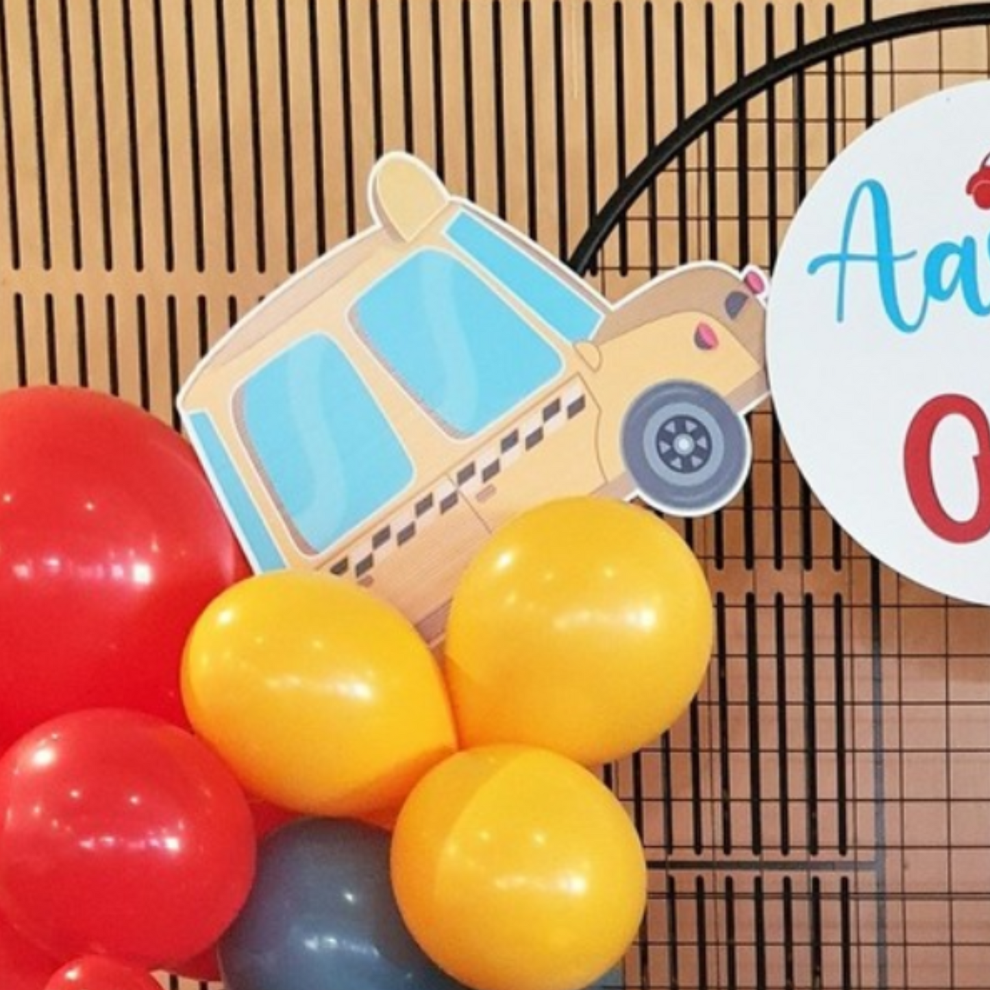 Colorful birthday party setup with red and yellow balloons, a cartoonish paper car decoration, and a circular sign with ‘Aarav’ written on it against a black grid background. Perfect for children’s birthday party themes and event styling ideas. Lush and Lavish Events