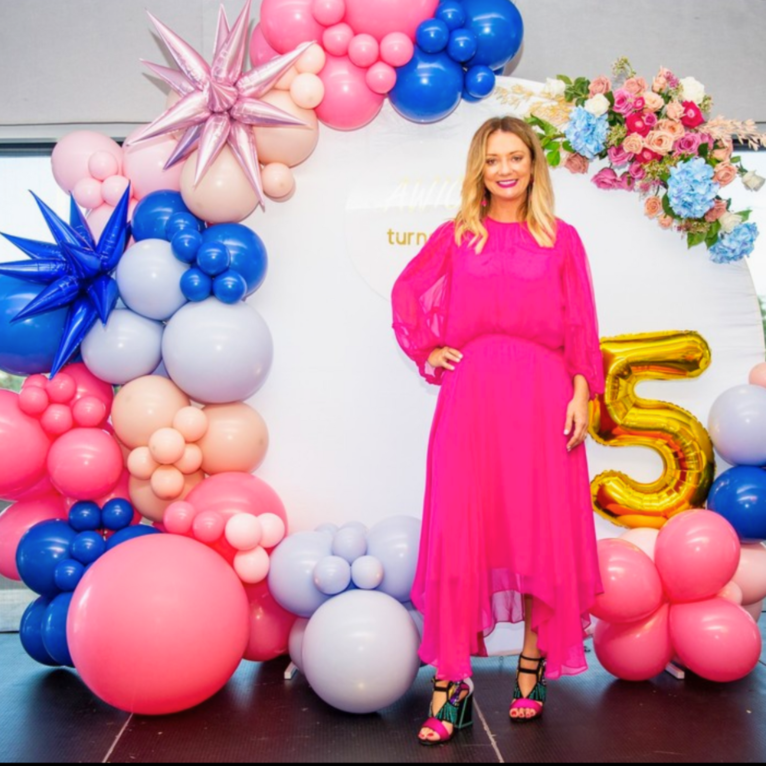 A person in a pink dress poses in front of a decorative balloon arch with metallic number "5" balloons. The backdrop features clusters of blue, pink, and white balloons, some shaped like stars. Prop hire, Prop hiring, Prop hire, event stylists Brisbane, brisbane event styling, brisbane event styling, event stylist Brisbane, Brisbane Wedding, Gold Coast Wedding, Floral Styling, Lush & Lavish Events, Brisbane Corporate Styling, Gold Coast Corporate Styling, Brisbane Brand Activation
