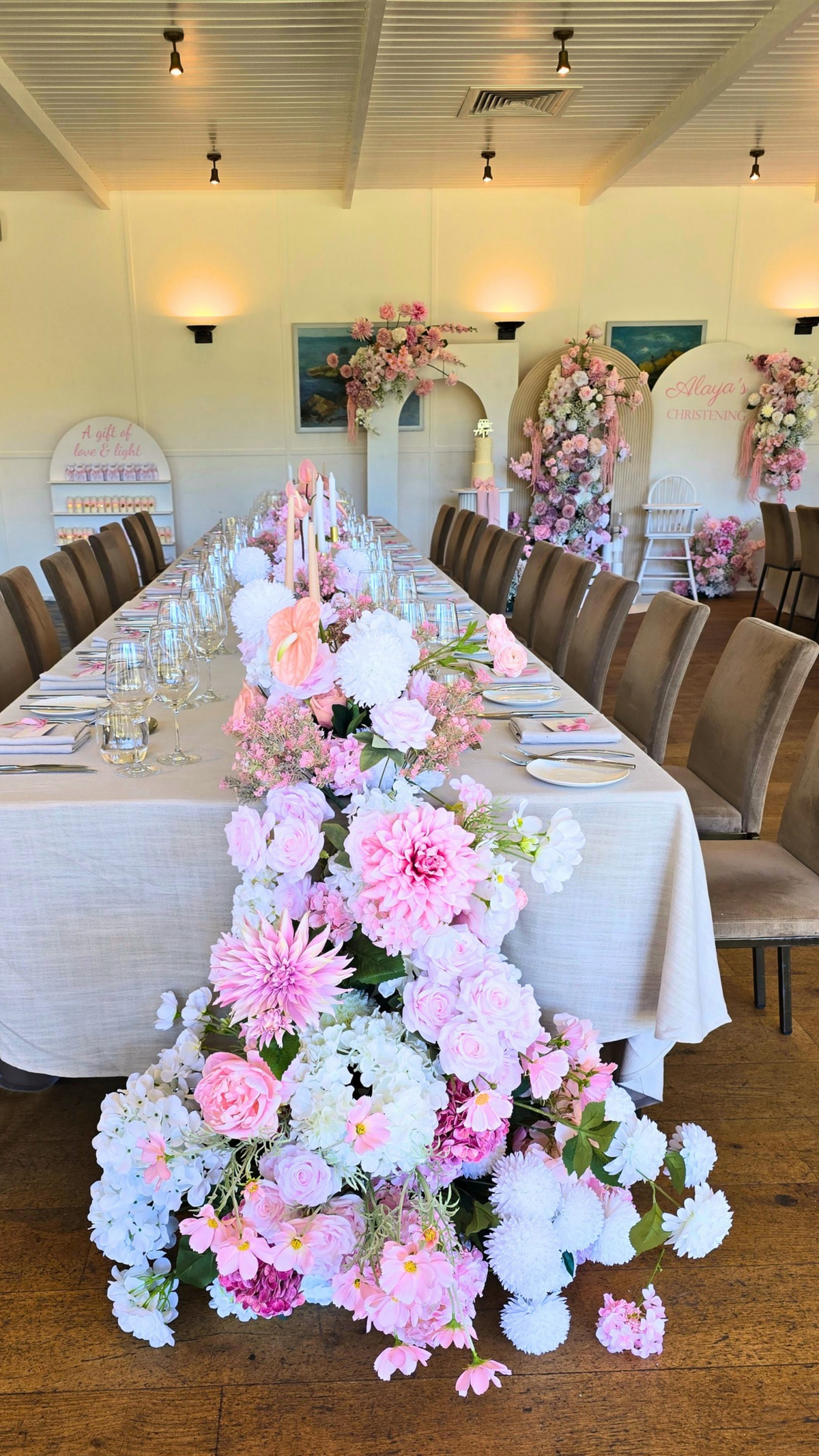 Decorative floral arrangement on a long table in a banquet hall with chairs and tables.