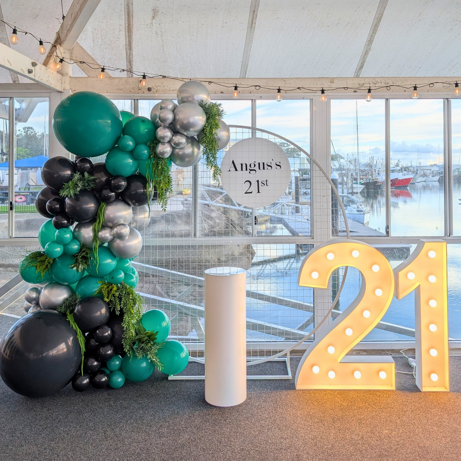 Lush green, silver and black 21st birthday balloon backdrop featuring a mesh arch, organic balloon garland with faux greenery accents and large illuminated LED number 21 lights. A luxury birthday party backdrop hire option perfect for 21st celebrations, milestone birthdays, photo opportunities and event styling across Brisbane, Gold Coast and South East Queensland.
