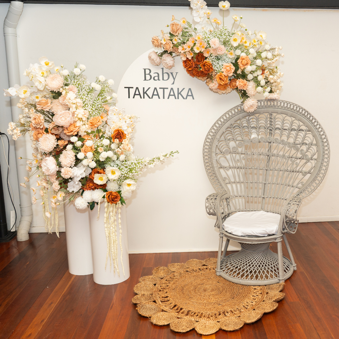 Decorative floral arrangements with a wicker chair on a wooden floor. baby shower backdrop, neutral floral backdrop, elegant event styling, Brisbane party hire, floral arch setup, engagement backdrop, birthday backdrop hire, custom event decor, neutral baby shower theme, white arch floral arrangement