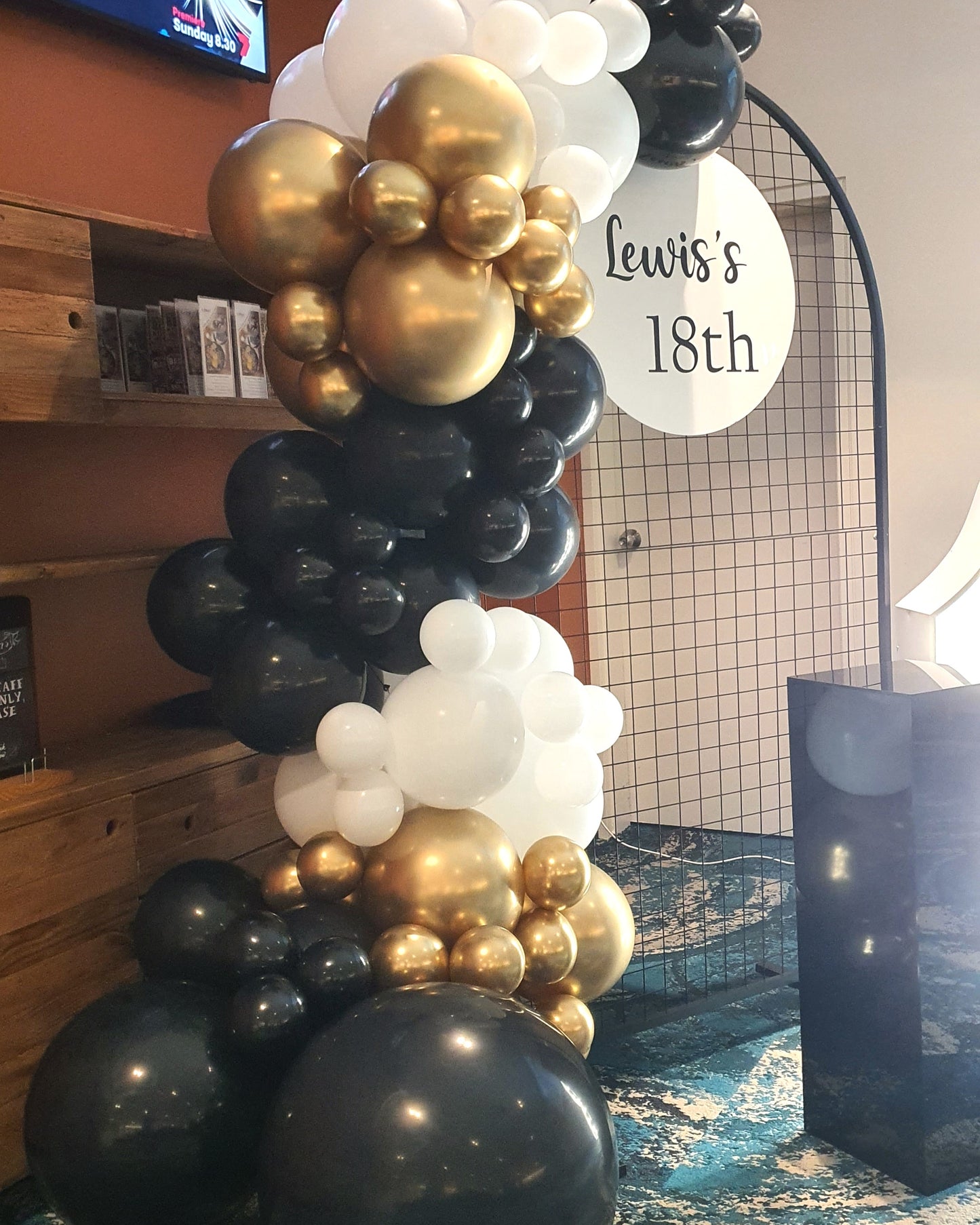 Balloon arrangement with black, white, and gold balloons around a circular sign that reads "Lewis's 18th." Prop hire, Prop hiring, Prop hire, event stylists Brisbane, brisbane event styling, brisbane event styling, event stylist Brisbane, Brisbane Wedding, Gold Coast Wedding, Floral Styling, Lush & Lavish Events, Brisbane Tablescape, Gold Coast Tablescapes, Brisbane Candle Hire