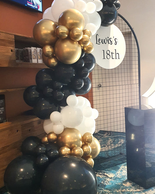 Balloon arrangement with black, white, and gold balloons around a circular sign that reads "Lewis's 18th." Prop hire, Prop hiring, Prop hire, event stylists Brisbane, brisbane event styling, brisbane event styling, event stylist Brisbane, Brisbane Wedding, Gold Coast Wedding, Floral Styling, Lush & Lavish Events, Brisbane Tablescape, Gold Coast Tablescapes, Brisbane Candle Hire