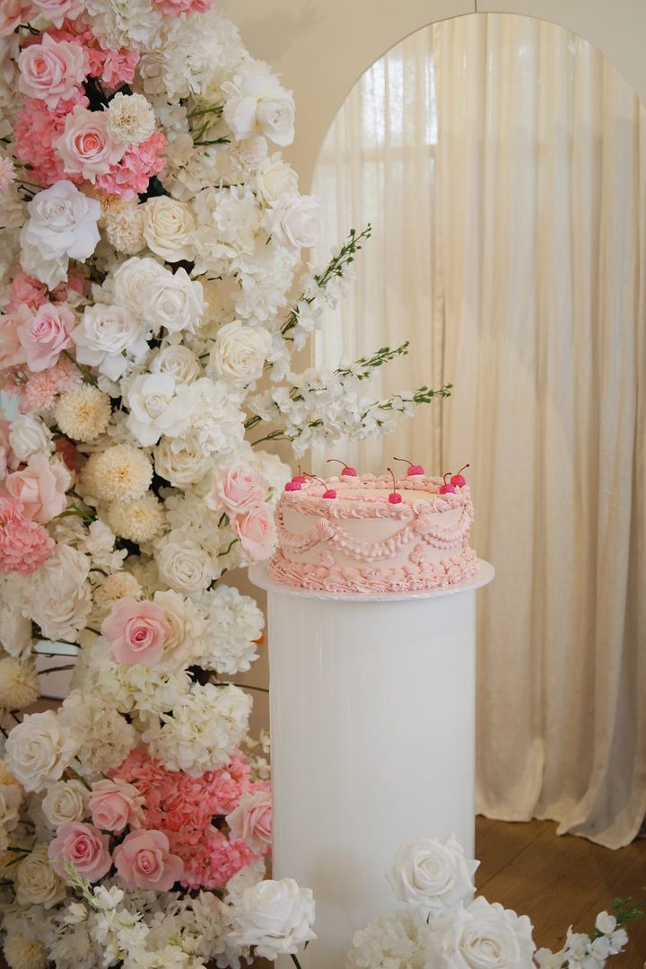 Pink cake with floral decorations on a white pedestal, against a floral backdrop. Prop hire, Prop hiring, Prop hire, event stylists Brisbane, brisbane event styling, brisbane event styling, event stylist Brisbane, Brisbane Wedding, Gold Coast Wedding, Floral Styling, Lush & Lavish Events, Brisbane Tablescape, Gold Coast Tablescapes, Brisbane Candle Hire