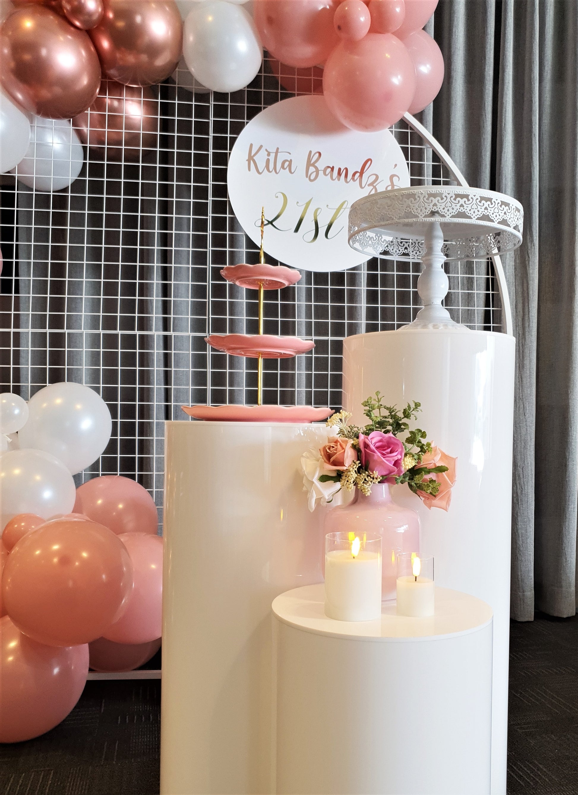 A balloon arch with white and pink balloons hangs over a dessert table with a three-tiered cake stand, candles, and a sign that says "Kita Bandz's 21st." Prop hire, Prop hiring, Prop hire, event stylists Brisbane, brisbane event styling, brisbane event styling, event stylist Brisbane, Brisbane Wedding, Gold Coast Wedding, Floral Styling, Lush & Lavish Events, Brisbane Tablescape, Gold Coast Tablescapes, Brisbane Candle Hire