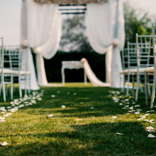 An outdoor wedding aisle with white chairs and rose petals on the grass, leading to a white draped archway with flowers. Prop hire, Prop hiring, Prop hire, event stylists Brisbane, brisbane event styling, brisbane event styling, event stylist Brisbane, Brisbane Wedding, Gold Coast Wedding, Floral Styling, Lush & Lavish Events