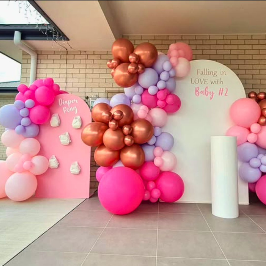 A baby shower backdrop featuring a large white arch with a balloon garland in shades of pink, purple, and rose gold, with the text ' Falling in LOVE with Baby #2' displayed. Backdrop by Lush and Lavish Events a Brisbane and Gold Coast based event styling, event planning and on-the-day coordination business.