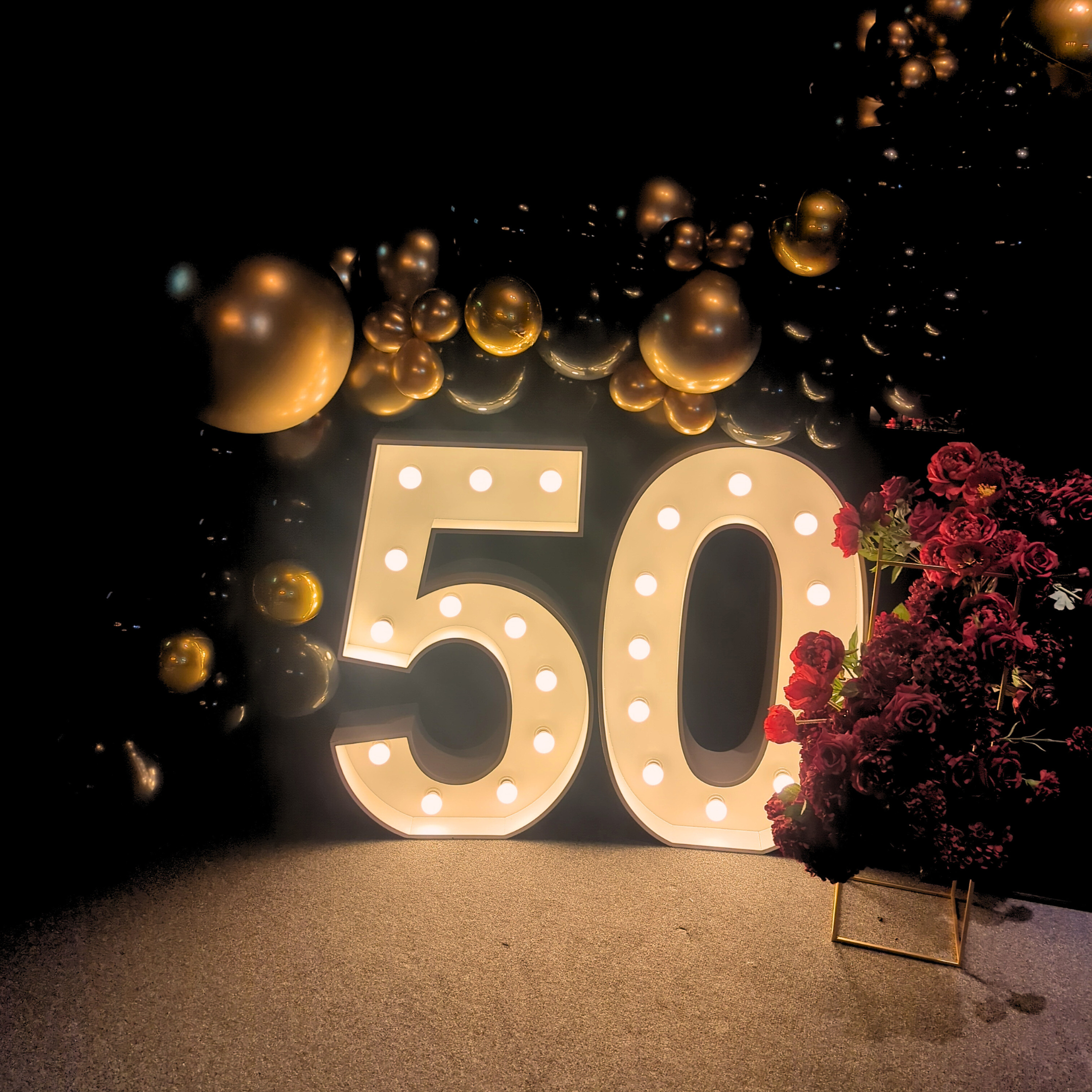 Illuminated '50' with golden balloons, red flowers, and a warm, dimly lit ambiance. Prop hire, Prop hiring, Prop hire, event stylists Brisbane, brisbane event styling, brisbane event styling, event stylist Brisbane, Brisbane Wedding, Gold Coast Wedding, Floral Styling, Lush & Lavish Events, Brisbane Tablescape, Gold Coast Tablescapes, Brisbane Candle Hire