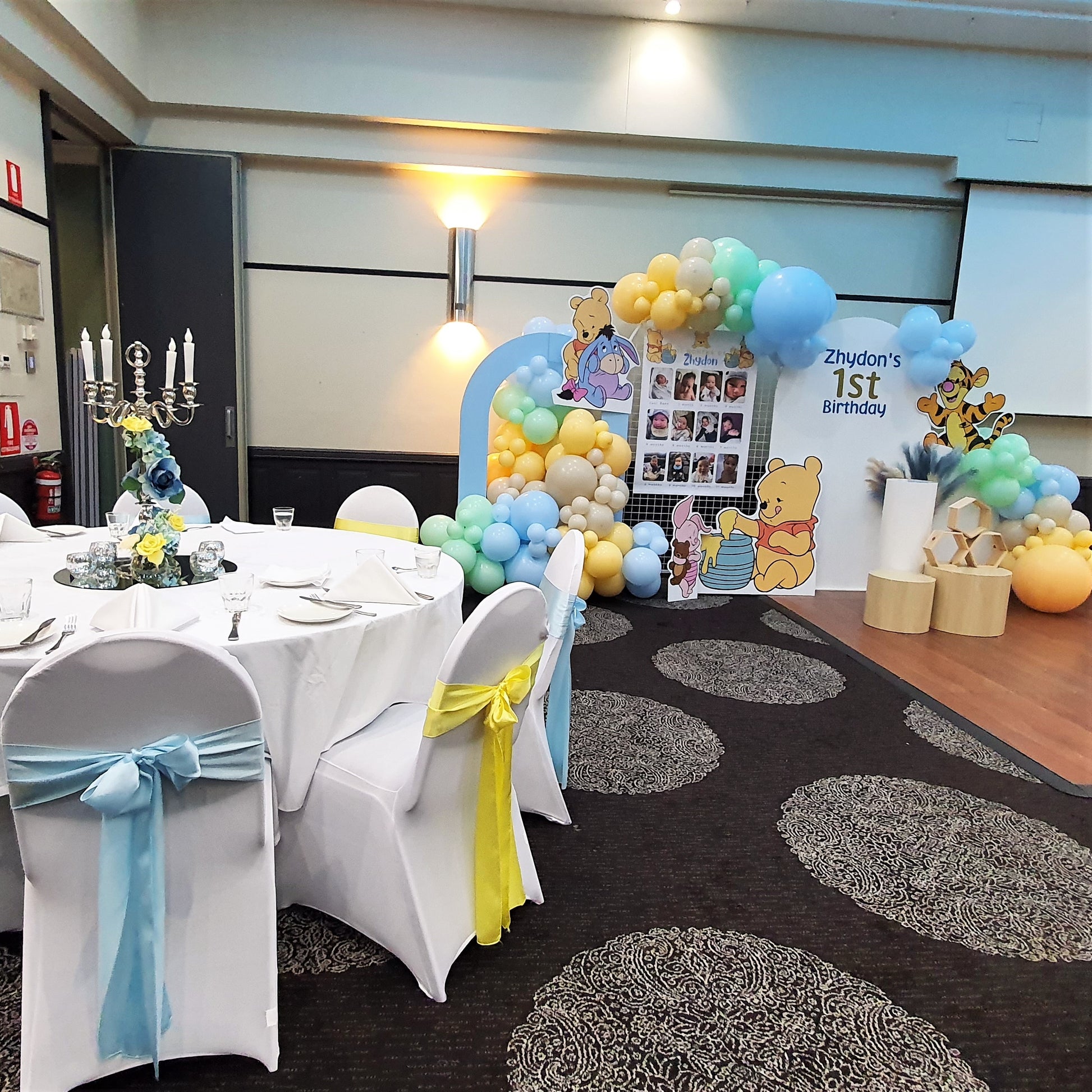 : A round table covered with a white tablecloth, surrounded by chairs with white covers and blue and yellow sashes. Prop hire, Prop hiring, Prop hire, event stylists Brisbane, brisbane event styling, brisbane event styling, event stylist Brisbane, Brisbane Wedding, Gold Coast Wedding, Floral Styling, Lush & Lavish Events