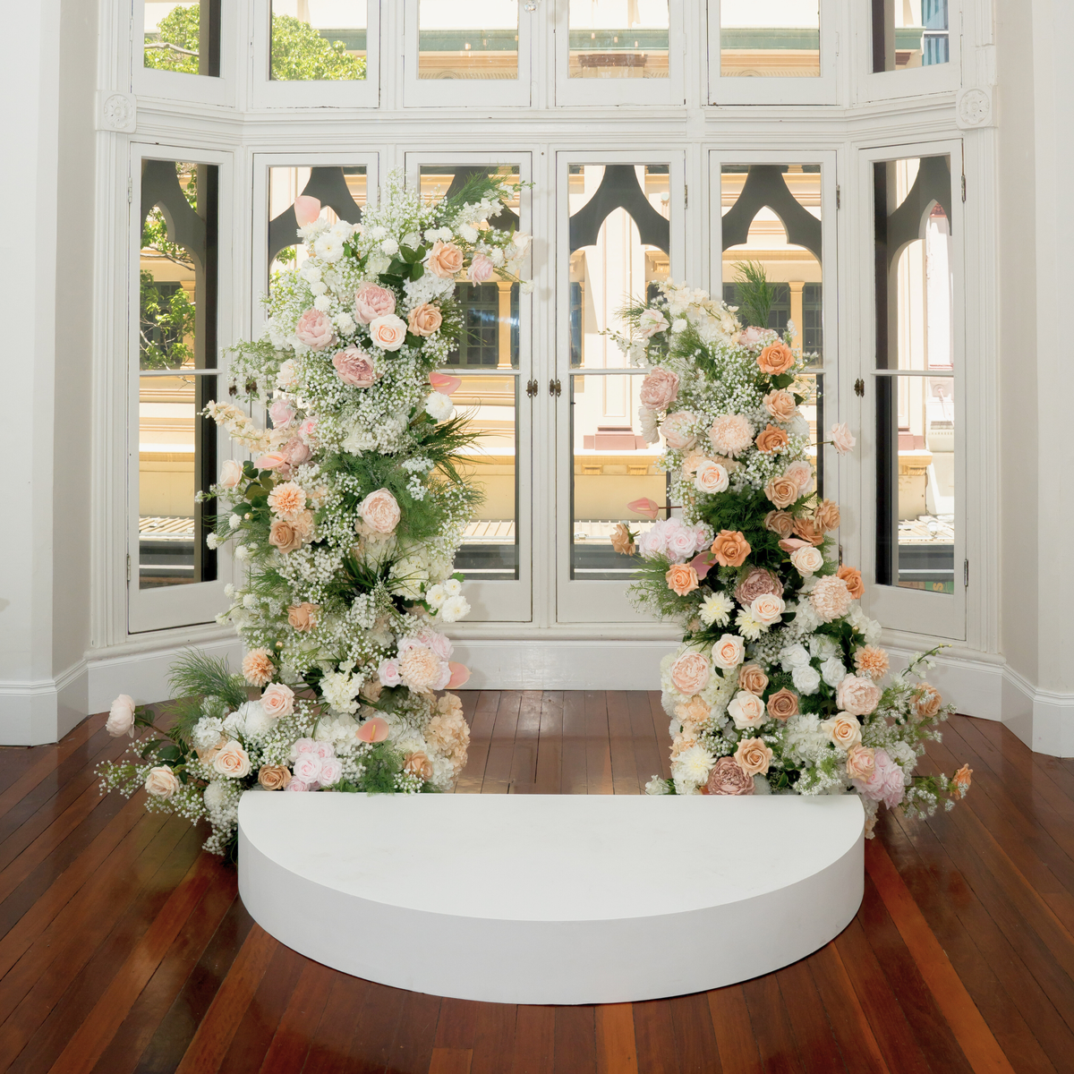 Floral arches decorated with white, pink, and orange flowers on a wooden floor. the little laneway wedding styling, the little laneway brisbane wedding venue styling, wedme brisbane wedding vendor, wedme co brisbane wedding trail, brisbane wedding styling, brisbane wedding stylist, luxury wedding styling brisbane, wedding ceremony styling brisbane, wedding reception styling brisbane, wedding altar styling brisbane, bridal table styling ideas, guest table wedding styling, wedding aisle styling ideas, wedding
