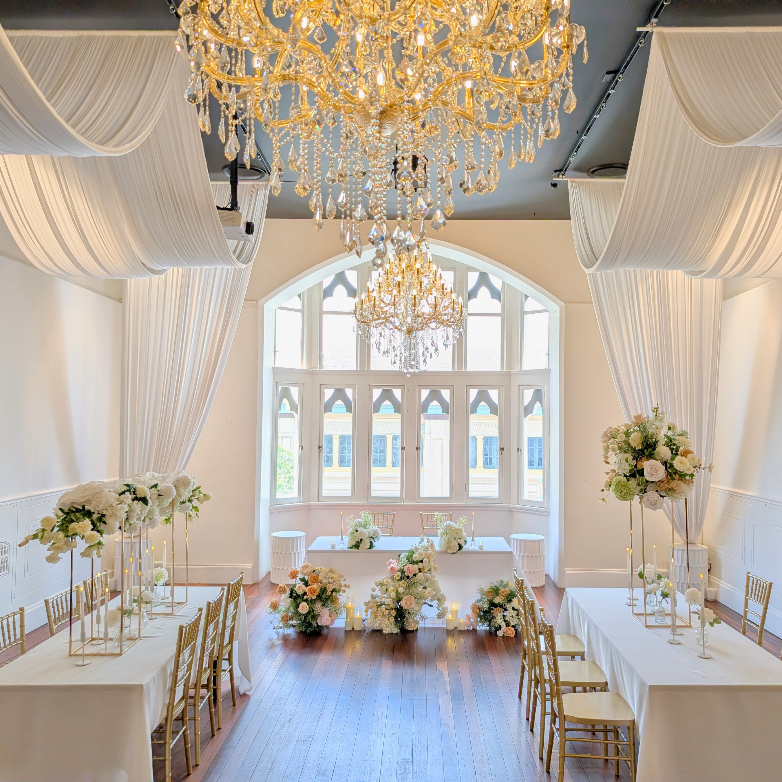 Elegant event venue with chandeliers, floral arrangements, and white drapes. the little laneway wedding styling, the little laneway brisbane wedding venue styling, wedme brisbane wedding vendor, wedme co brisbane wedding trail, brisbane wedding styling, brisbane wedding stylist, luxury wedding styling brisbane, wedding ceremony styling brisbane, wedding reception styling brisbane, wedding altar styling brisbane, bridal table styling ideas, guest table wedding styling, wedding aisle styling ideas.