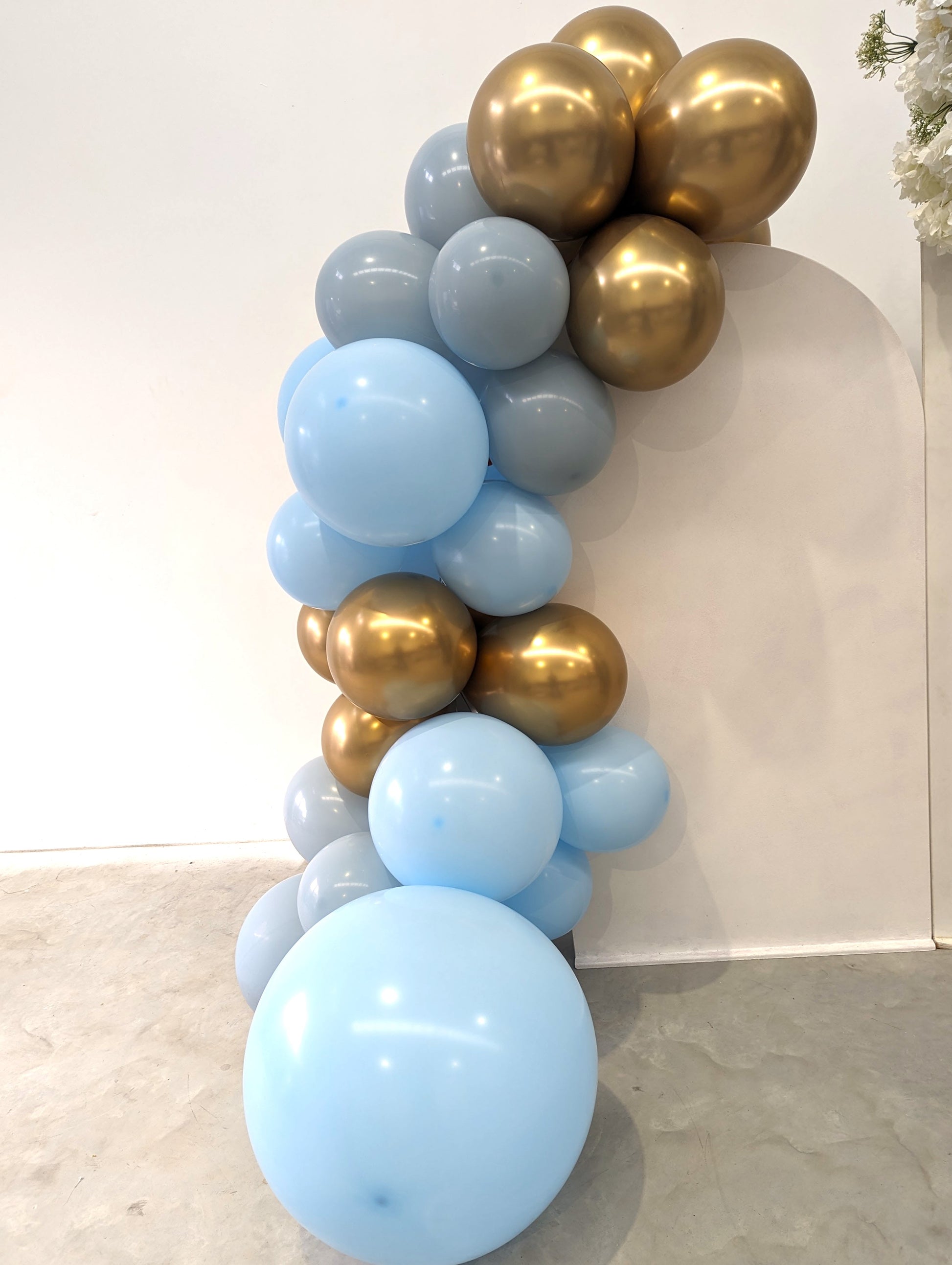 Balloon arrangement with light blue, gray, and gold balloons forming an arch against a white wall. Prop hire, Prop hiring, Prop hire, event stylists Brisbane, brisbane event styling, brisbane event styling, event stylist Brisbane, Brisbane Wedding, Gold Coast Wedding, Floral Styling, Lush & Lavish Events, Brisbane Corporate Styling, Gold Coast Corporate Styling, Brisbane Brand Activation