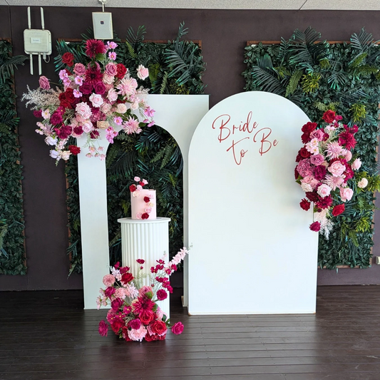 Decorative setup with floral arrangements and 'Bride to Be' sign. bridal shower backdrop, red and pink floral backdrop, elegant event styling, wedding backdrop hire, engagement party decor, Brisbane event hire, floral arch setup, romantic party backdrop, custom event decor, luxe bridal shower decorationsagainst a dark wall.