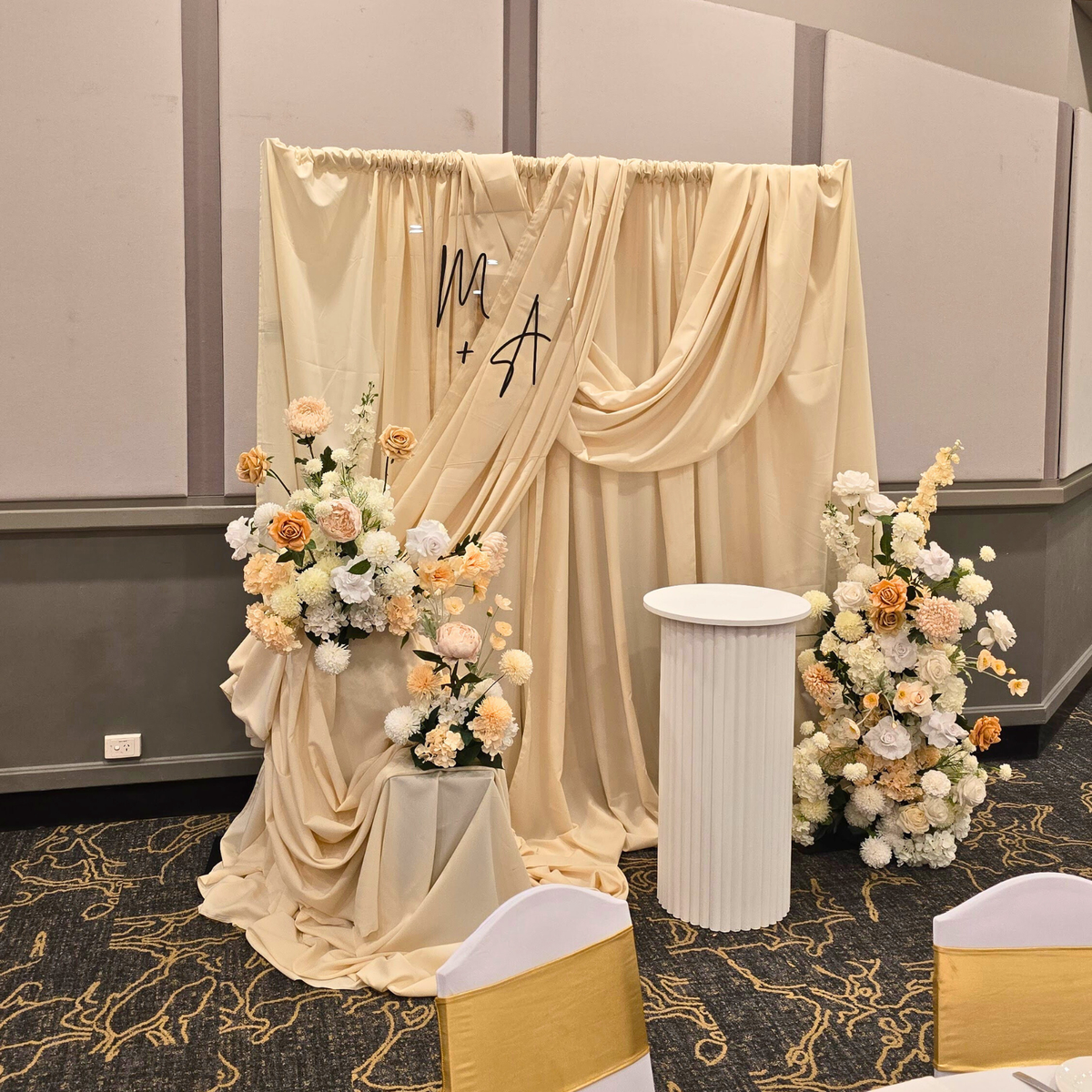 Decorative setup with floral arrangements and draped fabric in a room. engagement party backdrop, draped floral backdrop, romantic event styling, Brisbane event hire, elegant engagement decor, proposal backdrop hire, floral arch setup, wedding backdrop hire, custom event backdrop, luxe engagement party decorations