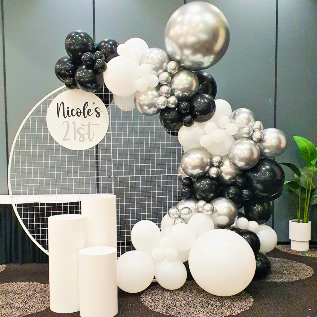 An elegant birthday balloon backdrop featuring a circular arch with black, silver, and white balloons, customized with a 'Nicole's 21st' acrylic sign. Styled by Lush and Lavish Events a Brisbane and Gold Coast based event planning, event styling, Event MC services and on-the-day coordination business.