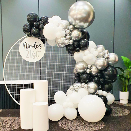An elegant birthday balloon backdrop featuring a circular arch with black, silver, and white balloons, customized with a 'Nicole's 21st' acrylic sign. Styled by Lush and Lavish Events a Brisbane and Gold Coast based event planning, event styling, Event MC services and on-the-day coordination business.