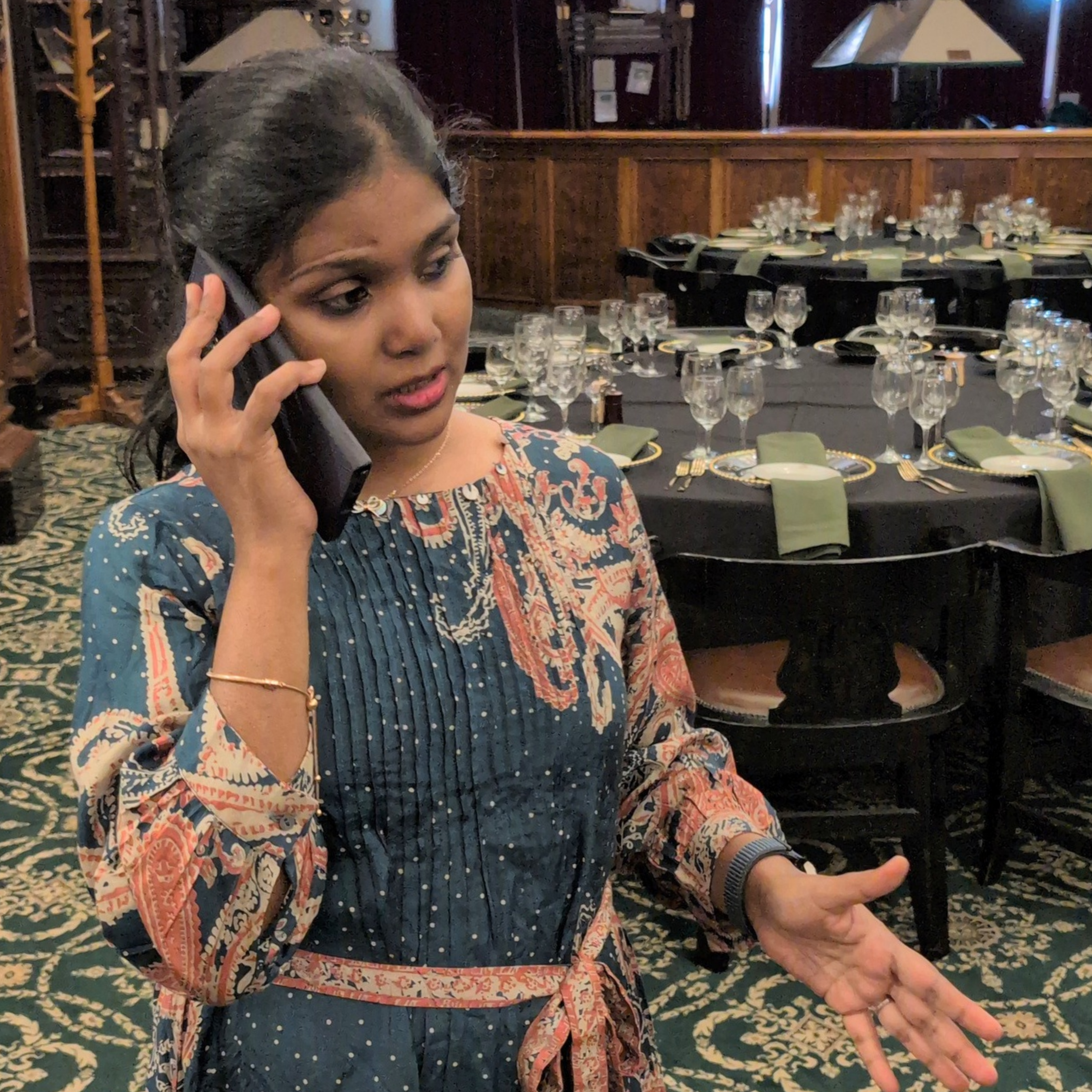 Woman talking on a phone in a formal event setting with tables and chairs. brisbane event styling, brisbane event planner, brisbane on the day coordination, brisbane 50th birthday styling, luxury event styling brisbane, brisbane birthday event planner, event stylist brisbane australia, brisbane venue styling ideas, elegant birthday styling brisbane, brisbane event design services, corporate event styling brisbane, brisbane party stylist, moody event styling brisbane, brisbane event coordination services, hi