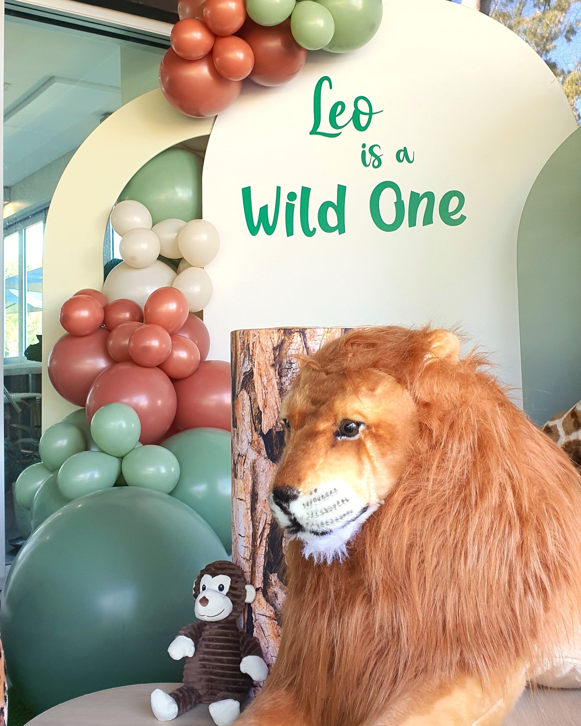 A safari-themed birthday party decoration with a balloon arch, a lion face cutout, and a monkey toy. Prop hire, Prop hiring, Prop hire, event stylists Brisbane, brisbane event styling, brisbane event styling, event stylist Brisbane, Brisbane Wedding, Gold Coast Wedding, Floral Styling, Lush & Lavish Events, Brisbane Tablescape, Gold Coast Tablescapes, Brisbane Candle Hire