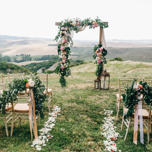Outdoor wedding ceremony setup with a floral arch and chairs decorated with greenery and flowers, overlooking a scenic landscape of rolling hills. Prop hire, Prop hiring, Prop hire, event stylists Brisbane, brisbane event styling, brisbane event styling, event stylist Brisbane, Brisbane Wedding, Gold Coast Wedding, Floral Styling, Lush & Lavish Events, Brisbane Tablescape, Gold Coast Tablescapes, Brisbane Candle Hire