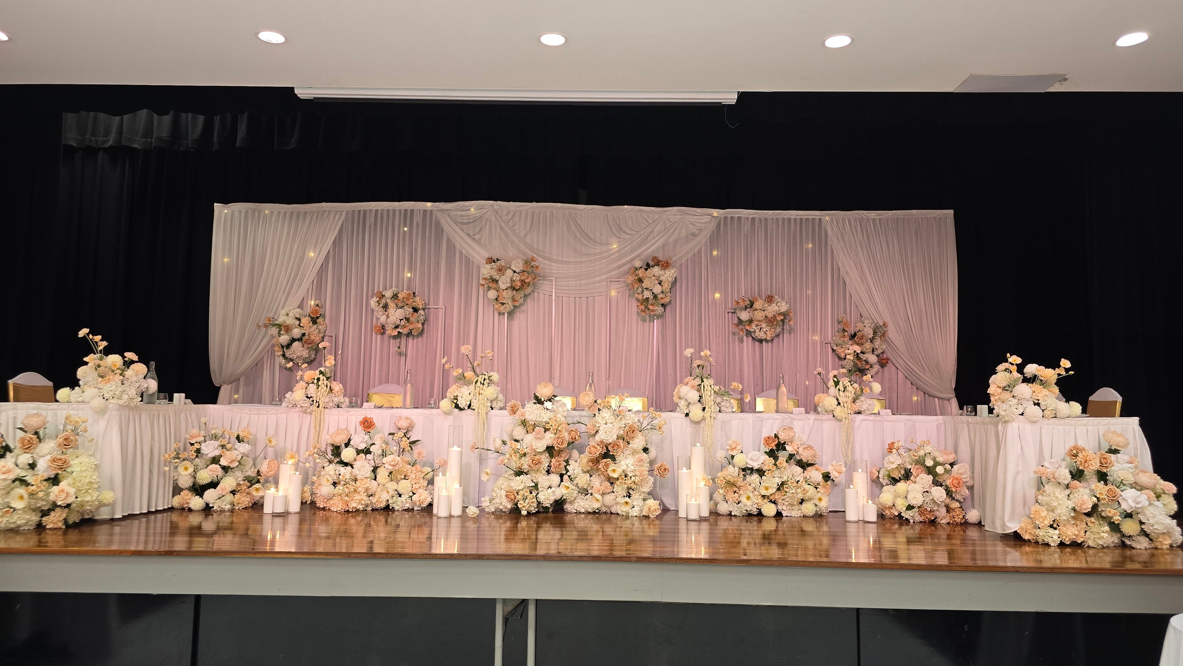 Decorated wedding reception table with floral arrangements against a dark backdrop. Decorations include lush and luxurious floral arrangements neatly and creatively arranged on top and base of the reception table. Includes table skirtings with impeccable background styling with white drapery and floral decorations.

Styled by Lush and Lavish events, Brisbane, gold coast, sunshine coast. Event styling gold coast, wedding gold coast, kedron wavell kittyhawk room styling, kedron wavell Chermside.