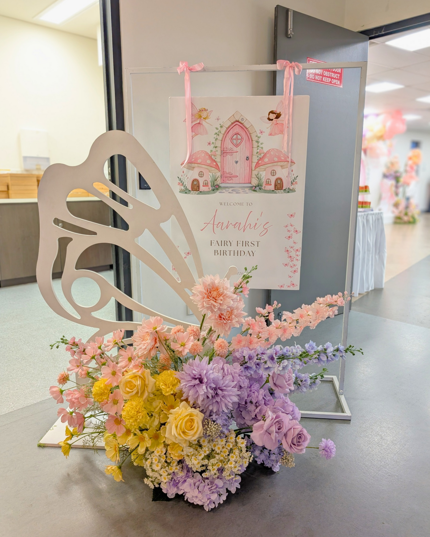Fairy first birthday butterfly themed welcome sign hire featuring a personalised A1 welcome poster on a white metal frame with ribbons, floral arrangement and large wooden butterfly cut out. Perfect for fairy first birthday parties, butterfly themed birthday celebrations, girls birthday decorations, kids party styling and magical event decor in Brisbane, Gold Coast and South East Queensland.
