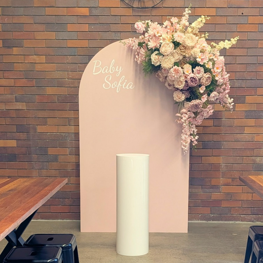A baby shower backdrop setup featuring a tall, light pink arch with the text 'Baby Sofia' in white script, decorated with a cascading floral arrangement of pink and cream roses, set against a rustic brick wall with a white acrylic plinth. Styled at Future Brewing Woolloongabba by Lush and Lavish Events a Brisbane and Gold coast based Event styling, event planning, on-the-day coordination and Event MC services business.
