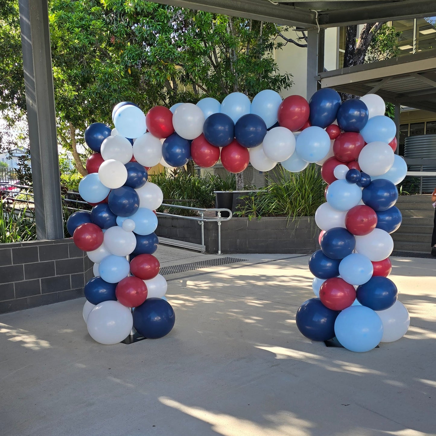 Balloon arch in red, white, and blue under a covered outdoor area. organic balloon arch, corporate balloon arch, balloon arch Brisbane, balloon arch Gold Coast, corporate event styling Brisbane, brand activation balloons, product launch balloons, media wall balloon arch, event backdrop Brisbane, event backdrop Gold Coast, branded balloon arch, PR event balloons, company event decorations, business event balloons, balloon garland Brisbane, luxury balloon styling, corporate event hire Brisbane, corporate even