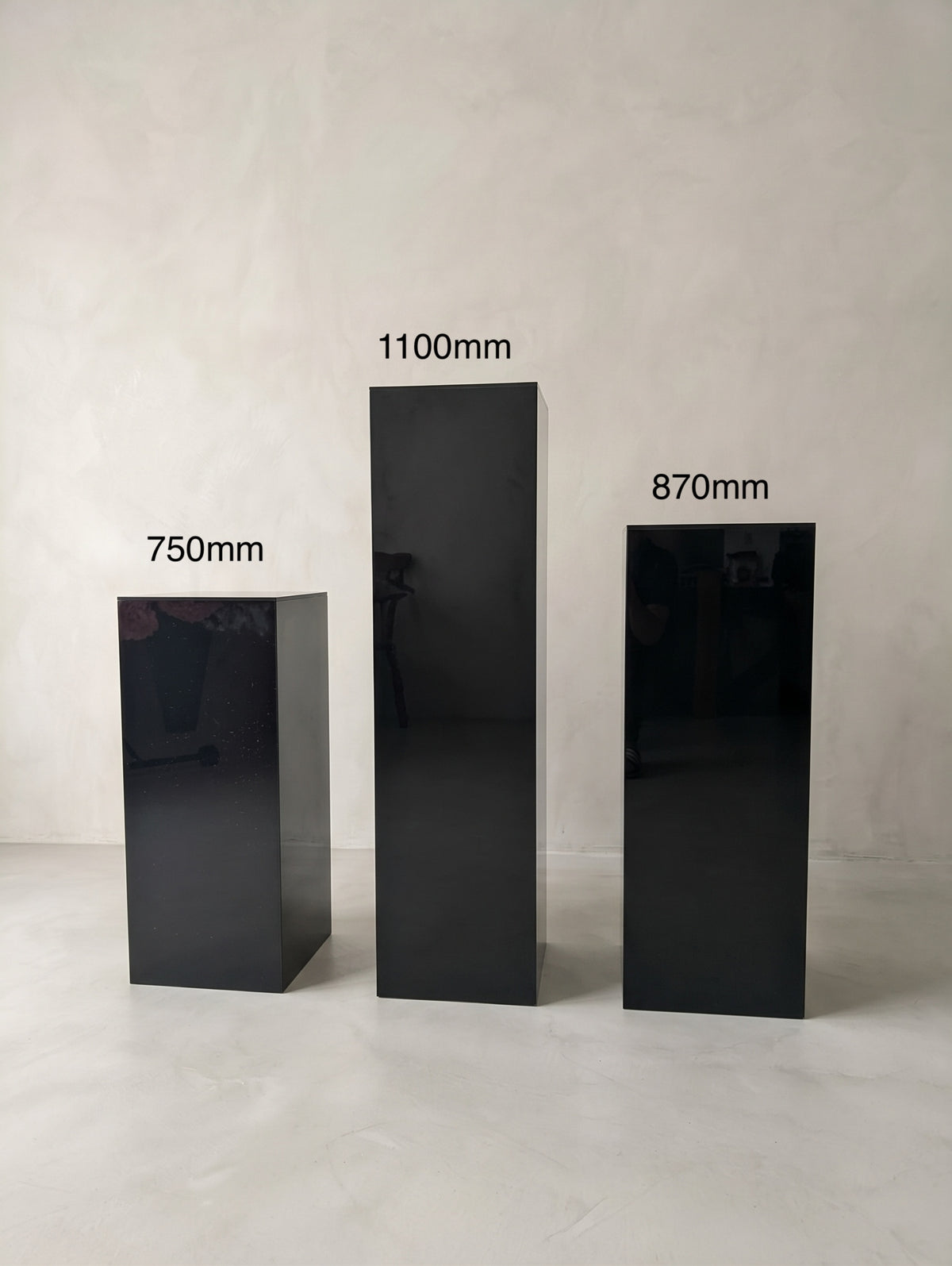 Three glossy black rectangular plinths with heights of 1100 mm, 870 mm and 750 mm.