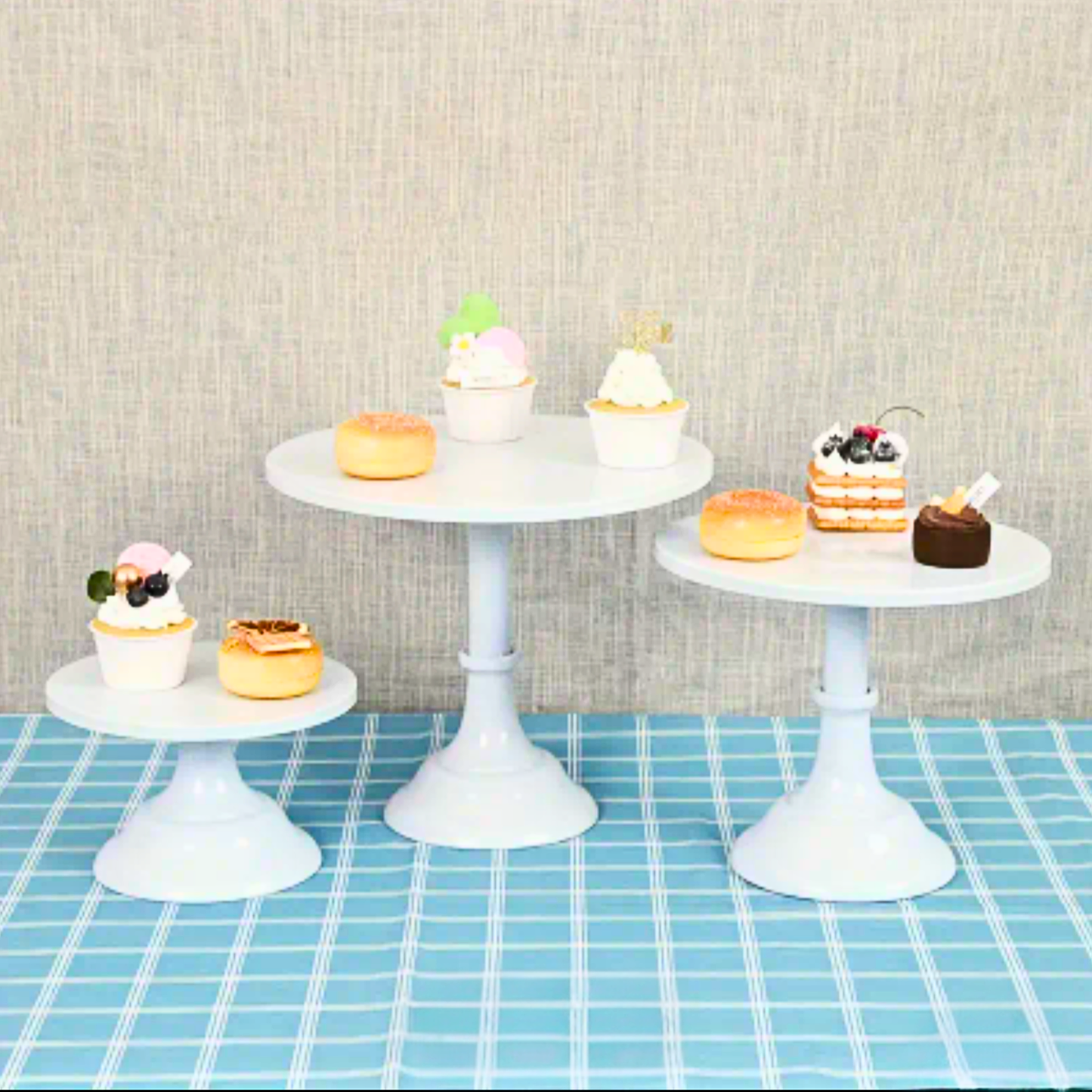 Set of white cake stands with small desserts on a checkered tablecloth. white cake stand, cake stand set, dessert display, tiered cake stand, wedding cake stand, birthday cake stand, cupcake stand, party hire Brisbane, party hire Gold Coast, cake table display, event hire Brisbane, event hire Gold Coast, celebration tableware, elegant cake stand, white dessert stand, cake display hire, table centrepiece stand, cake presentation, party styling Brisbane, party styling Gold Coast