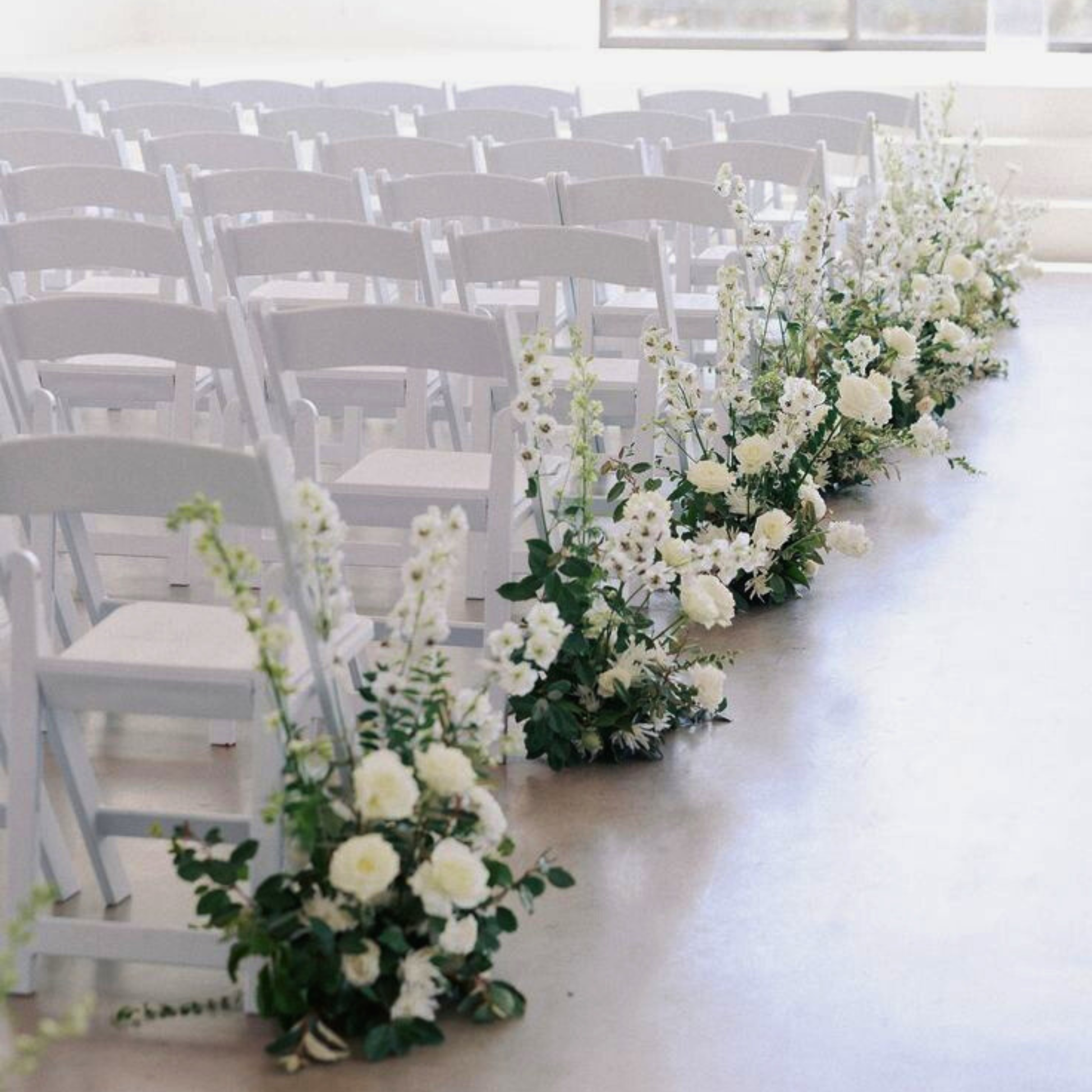 White floral arrangements lining a wedding aisle with white chairs. wedding aisle markers hire, floral aisle markers hire, wedding aisle flowers hire, DIY wedding aisle decor, wedding ceremony decor hire, aisle flowers for wedding, wedding flowers hire Brisbane, Brisbane wedding hire decor, wedding aisle decor Brisbane, Gold Coast wedding hire, wedding flowers hire Gold Coast, DIY wedding flowers, ceremony aisle styling, wedding aisle arrangements, modern wedding decor hire, organic wedding florals, wedding