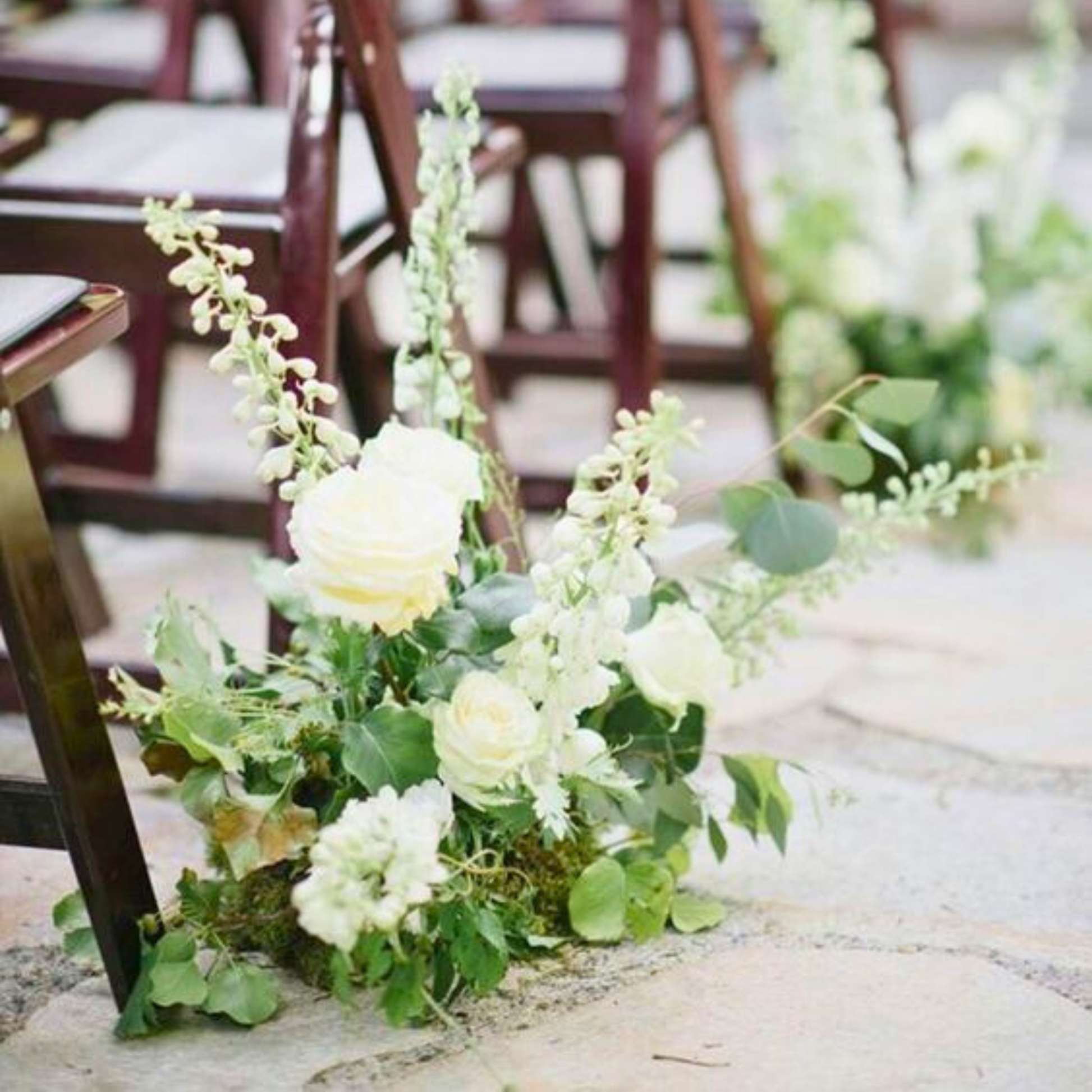 Floral arrangement on a stone pathway with wooden chairs in the background. wedding aisle markers hire, floral aisle markers hire, wedding aisle flowers hire, DIY wedding aisle decor, wedding ceremony decor hire, aisle flowers for wedding, wedding flowers hire Brisbane, Brisbane wedding hire decor, wedding aisle decor Brisbane, Gold Coast wedding hire, wedding flowers hire Gold Coast, DIY wedding flowers, ceremony aisle styling, wedding aisle arrangements, modern wedding decor hire, organic wedding florals,