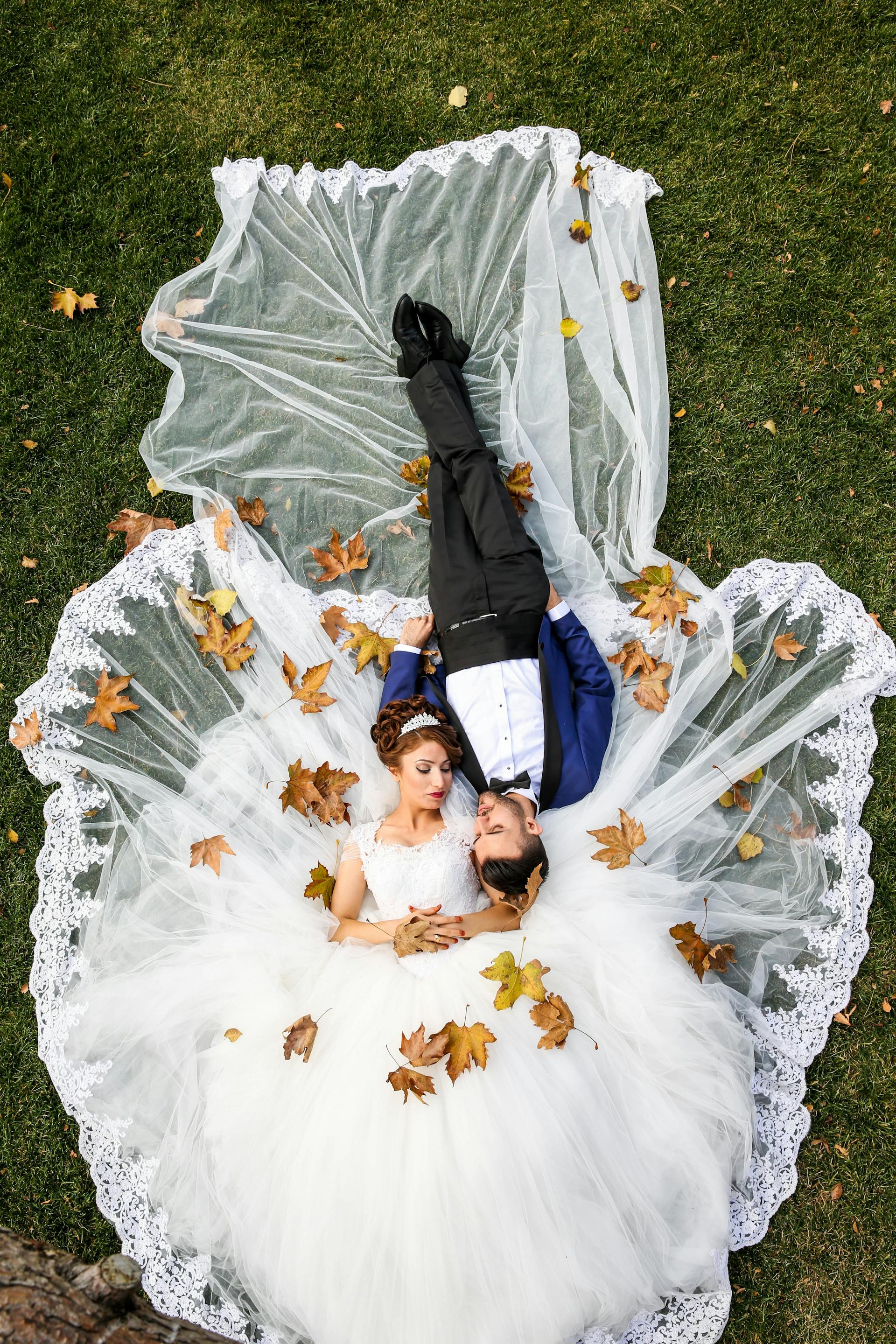 Couple lying on grass with autumn leaves on bride's dress, holding hands. Prop hire, Prop hiring, Prop hire, event stylists Brisbane, brisbane event styling, brisbane event styling, event stylist Brisbane, Brisbane Wedding, Gold Coast Wedding, Floral Styling, Lush & Lavish Events, Brisbane Corporate Styling, Gold Coast Corporate Styling, Brisbane Brand Activation