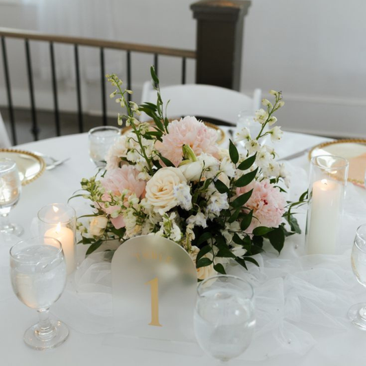 Decorative table setting with flowers, candles, and glasses on a white tablecloth.
