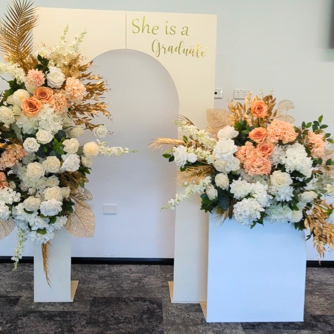White arches with lush floral arrangements with signage "She is a Graduate". Prop hire, Prop hiring, Prop hire, event stylists Brisbane, brisbane event styling, brisbane event styling, event stylist Brisbane, Brisbane Wedding, Gold Coast Wedding, Floral Styling, Lush & Lavish Events, Brisbane Corporate Styling, Gold Coast Corporate Styling, Brisbane Brand Activation, Gold Coast Tablescapes, Brisbane Candle Hire